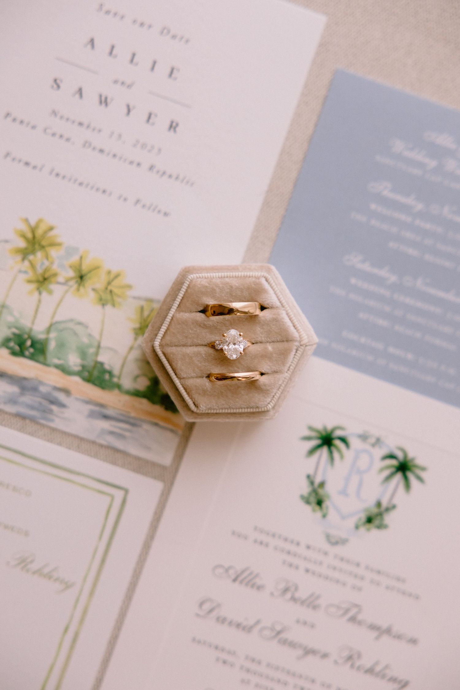 Gold wedding rings in a velvet hexagon box atop elegant wedding invitations for Allie and Sawyer.