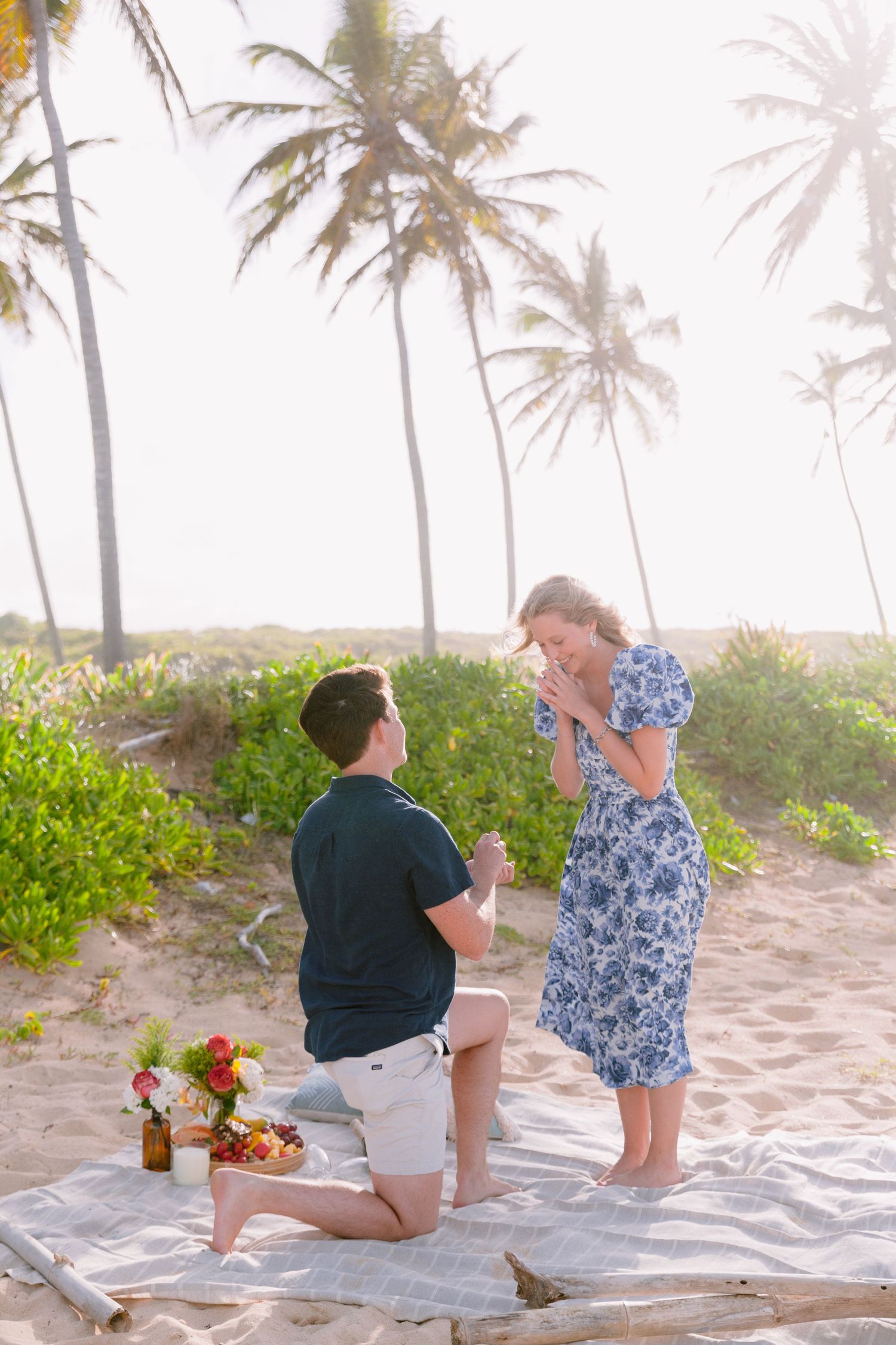 A romantic beach proposal scene with palm trees in the background as a couple shares a special moment on the sand.