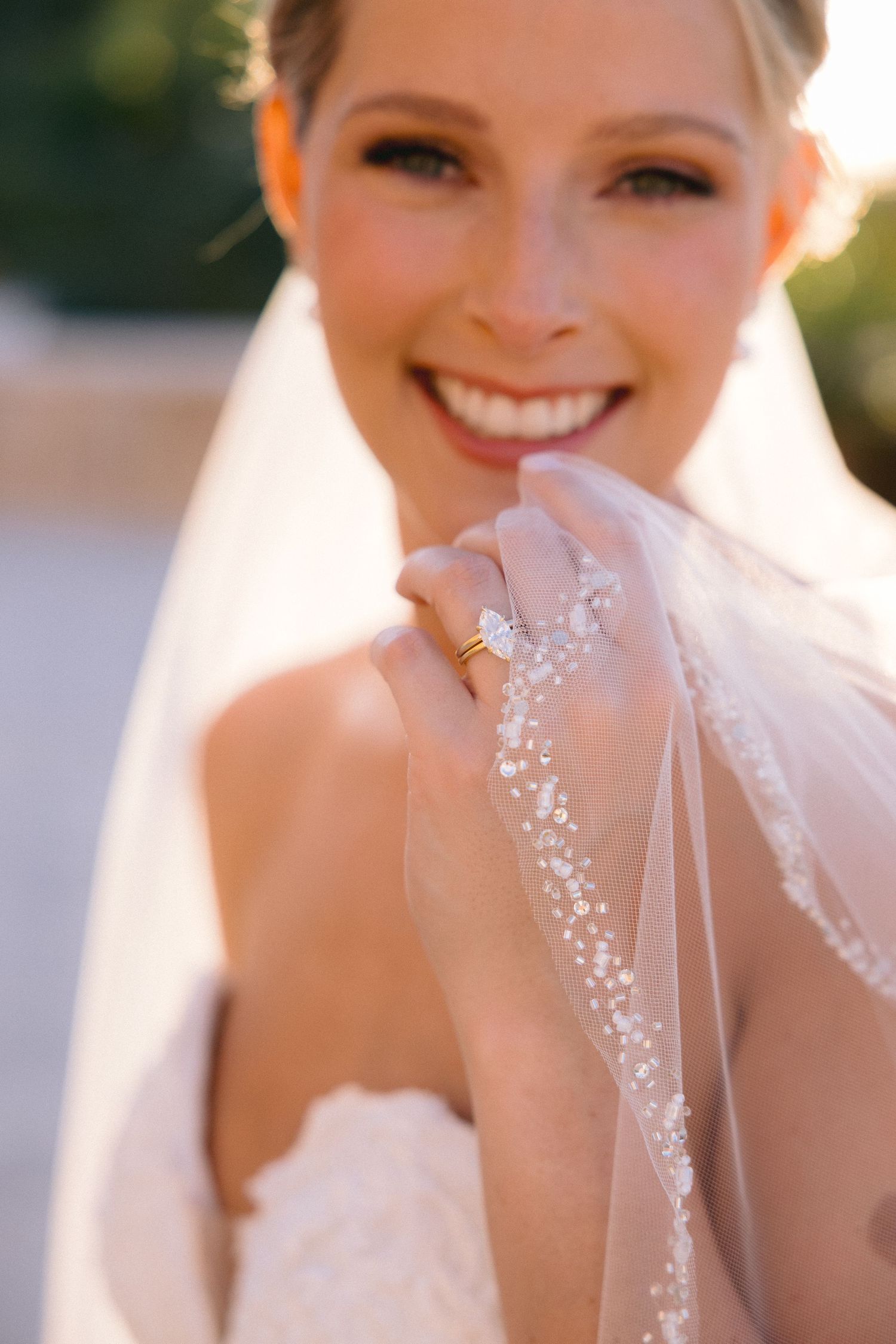 A bride in a white wedding dress with a delicate veil poses in soft sunlight during her wedding photoshoot.