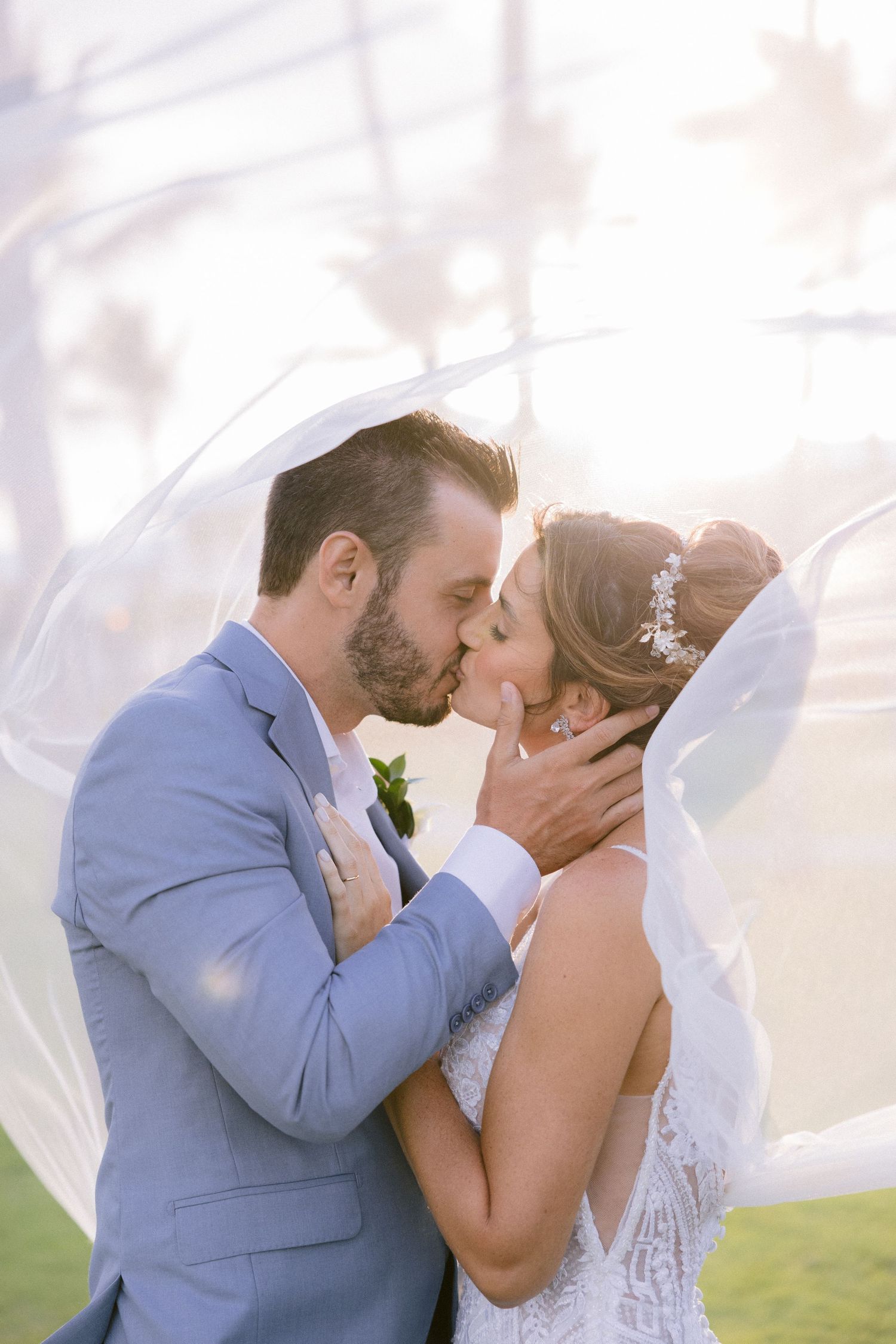 A romantic wedding kiss captured under flowing veil with soft lighting.