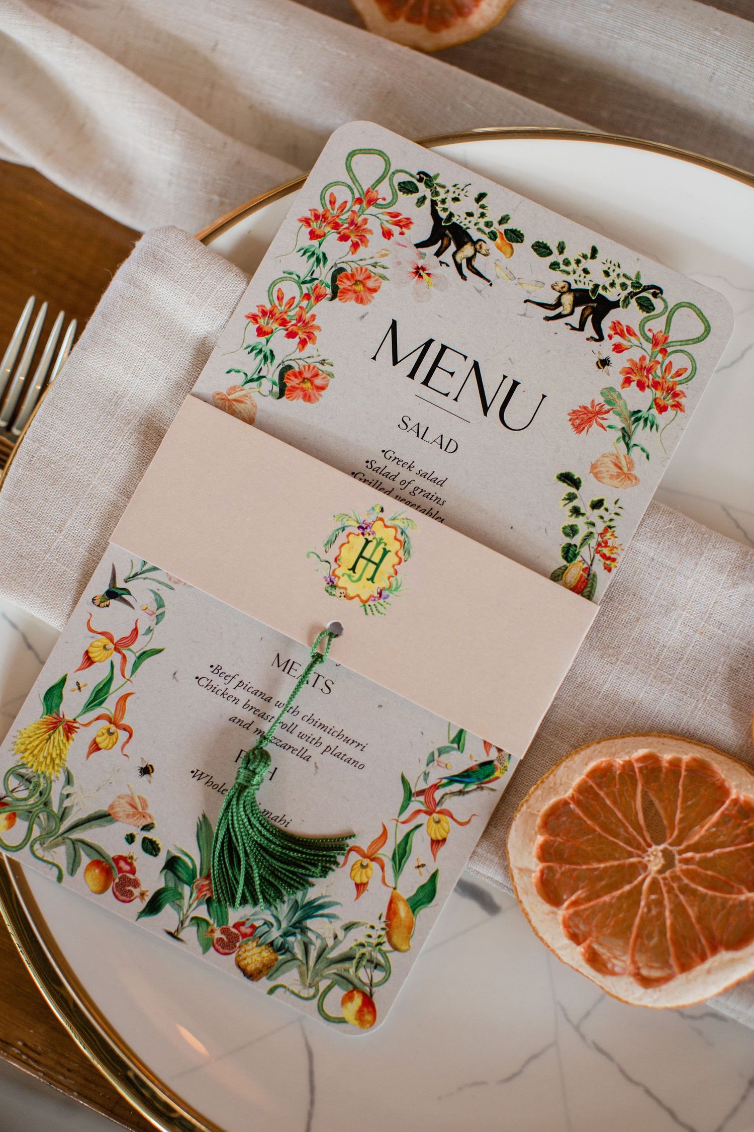 Menu cards decorated with delicate floral designs are displayed alongside dried orange slices on a white tablecloth.