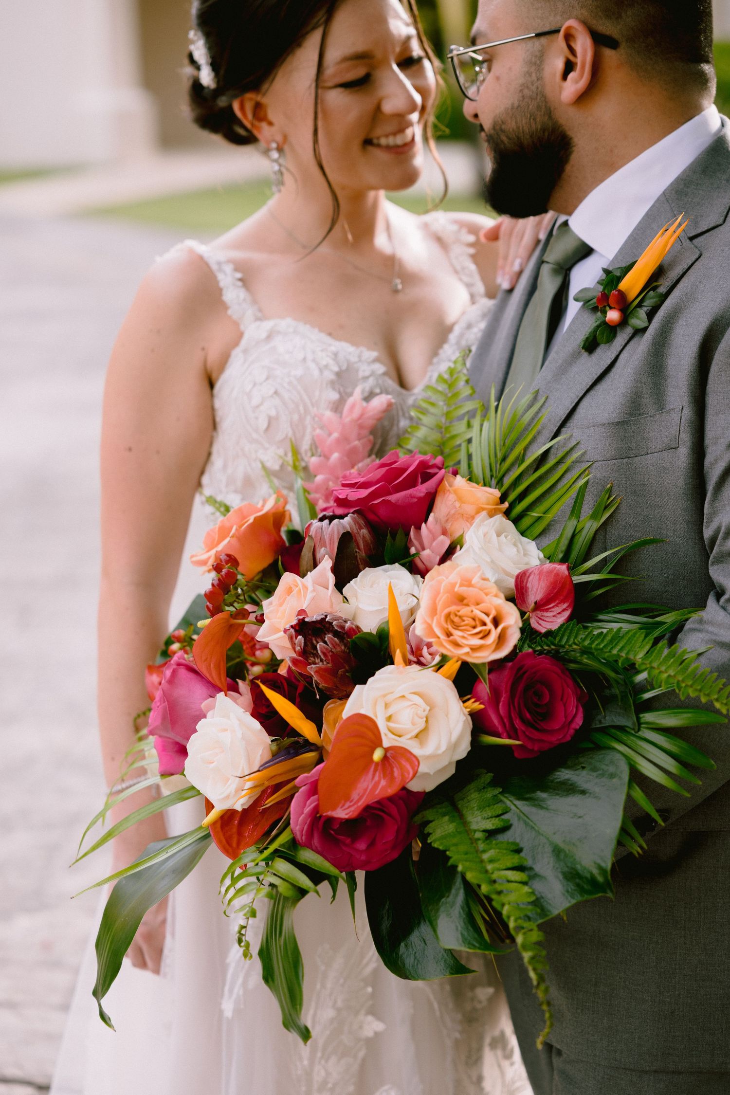 A romantic wedding moment with a vibrant tropical bouquet featuring red and peach roses, palm fronds and orange lilies.