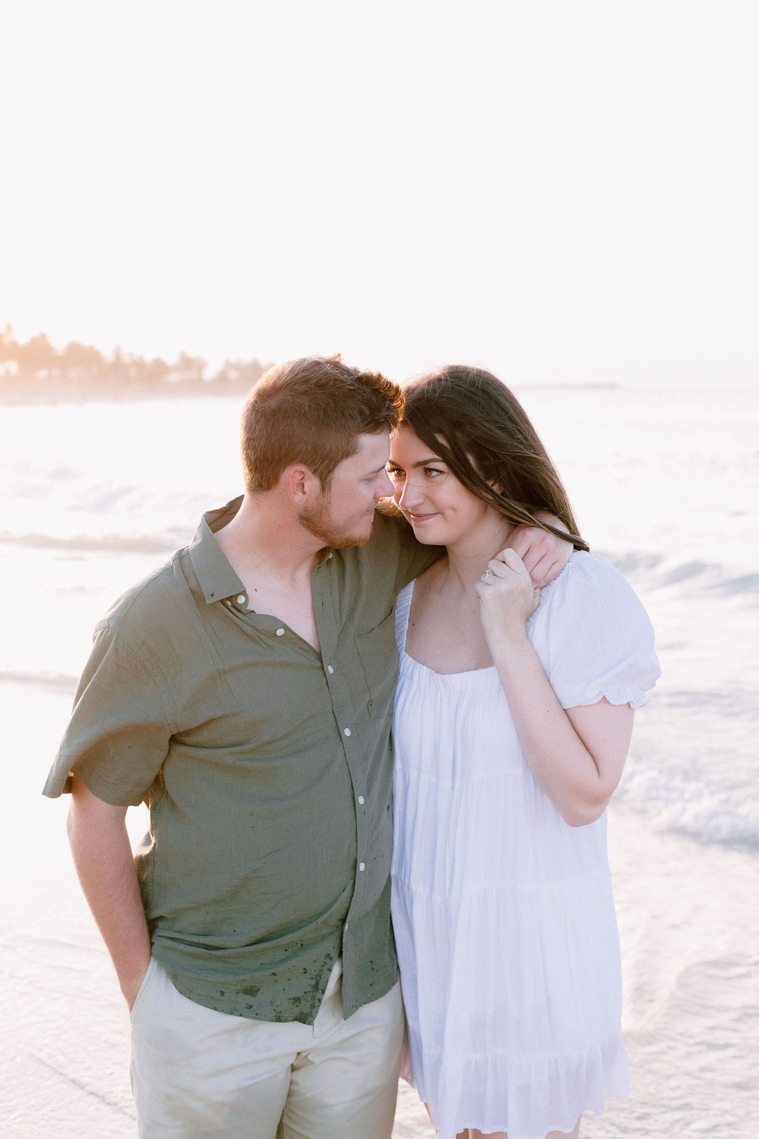 Intimate moment between couple in white and grey clothing on beach at sunset.