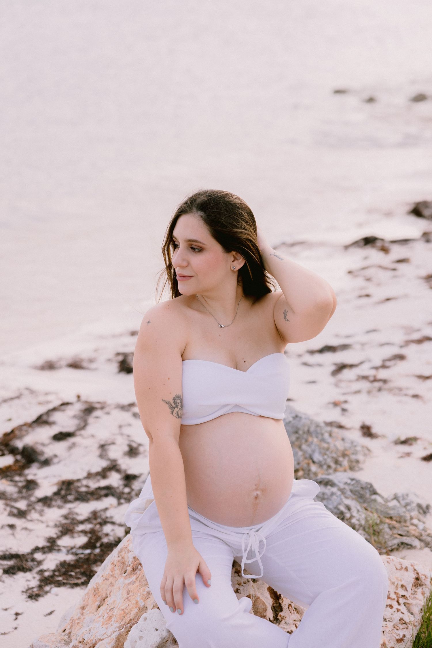 Woman in white two-piece outfit posing on rocky beach setting.