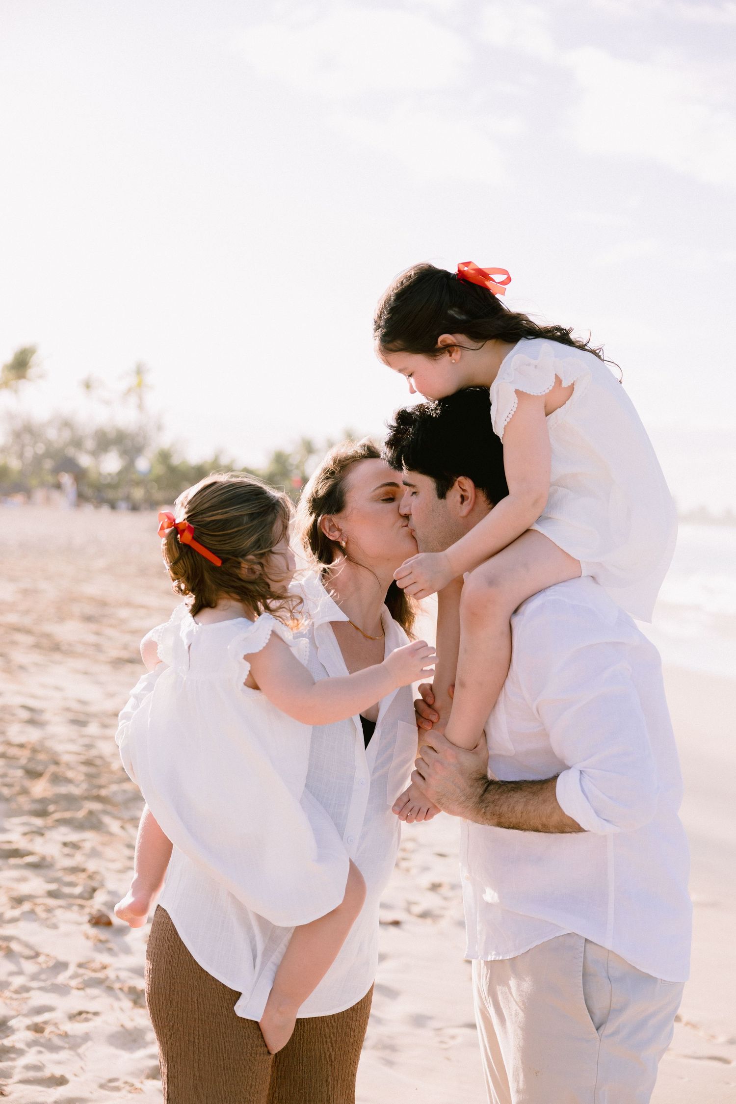 A family wearing white clothing shares tender moments together on a sunny beach.