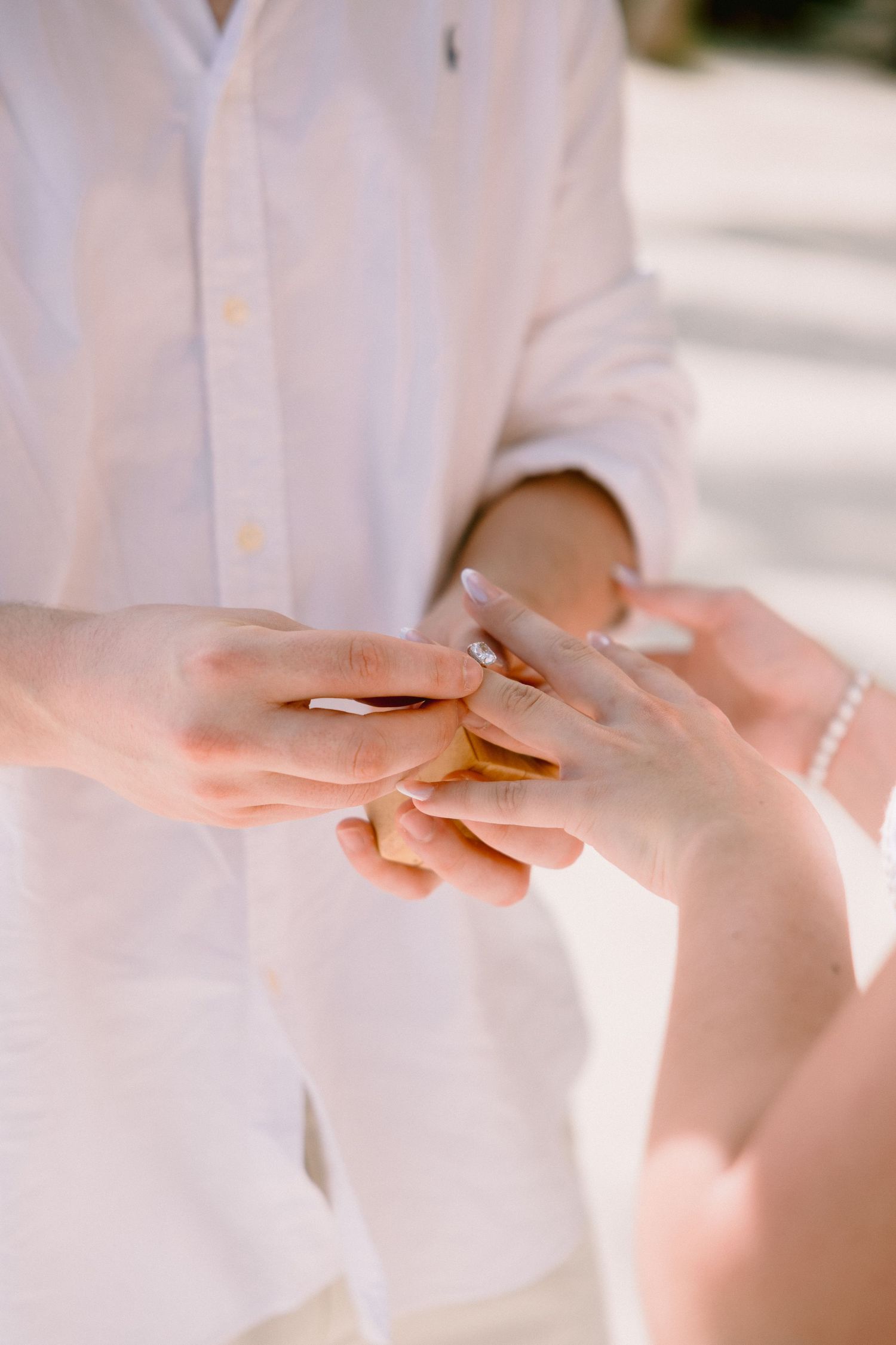Close-up of hands exchanging wedding rings during an intimate ceremony, with one person wearing a white dress shirt.