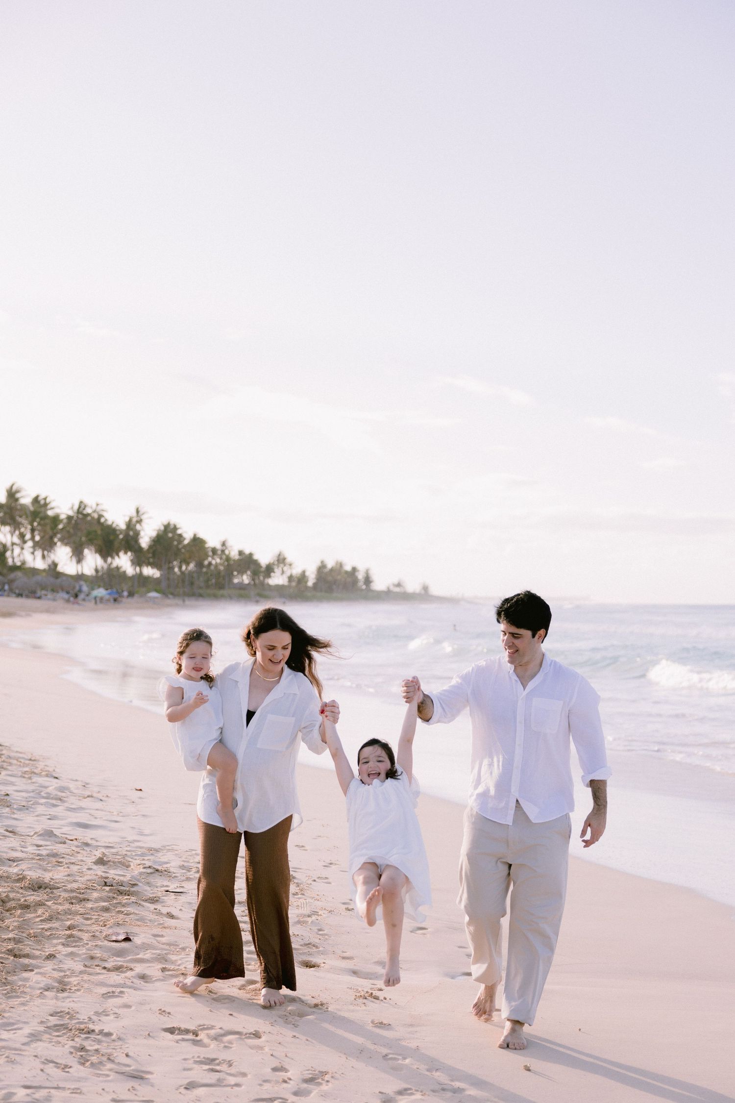 A family walks together on a tropical beach at sunset with palm trees in the background.