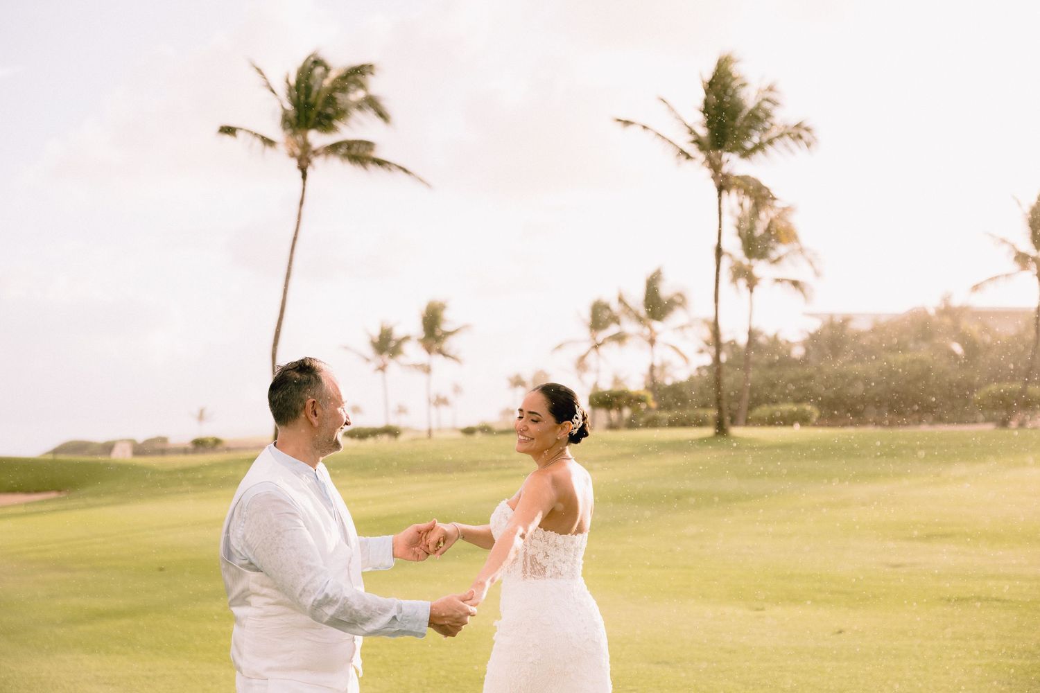 A couple shares a romantic moment on a beach at sunset with palm trees swaying in the background.