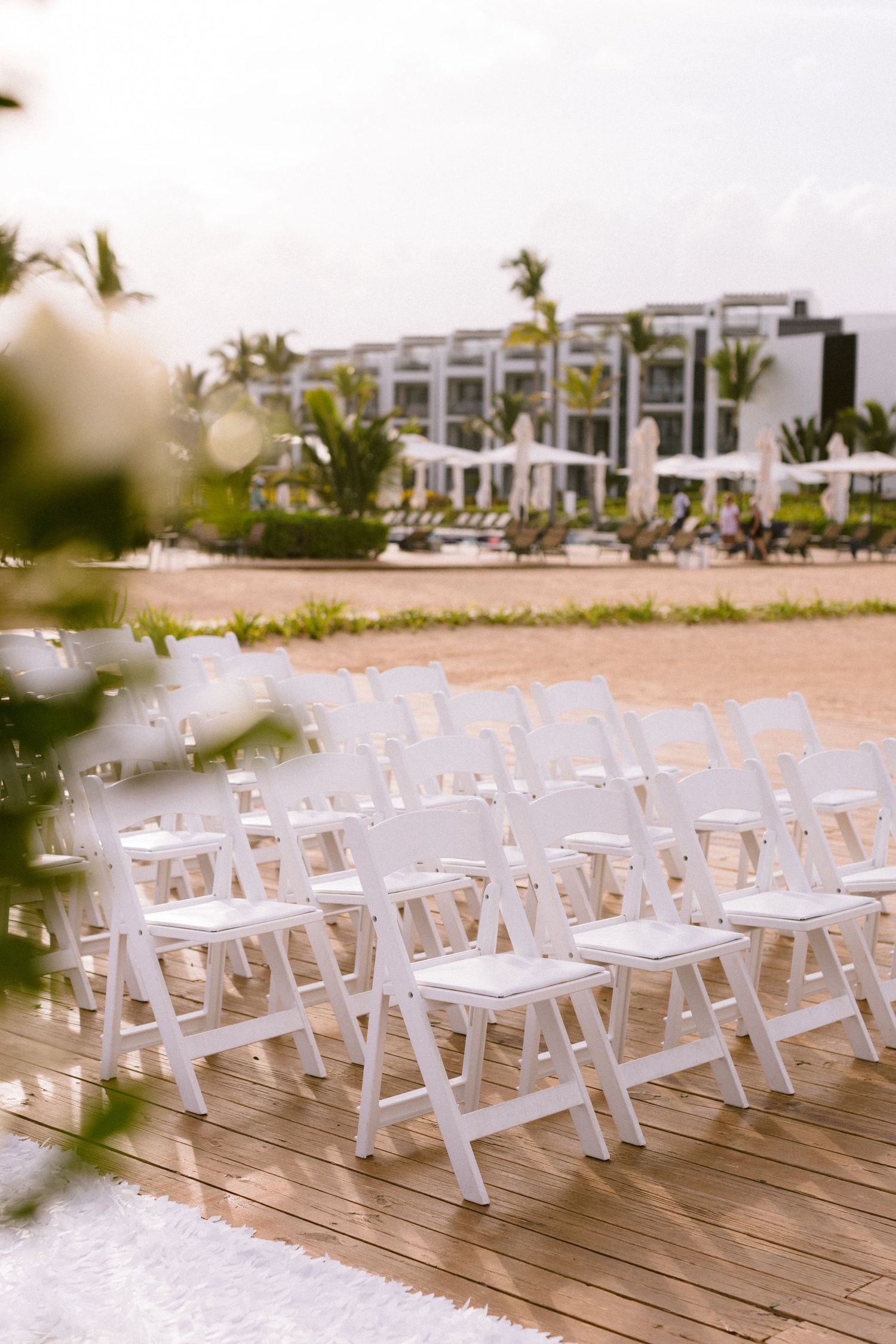 White folding chairs arranged in rows on a wooden deck for an outdoor beach wedding ceremony at a tropical resort.