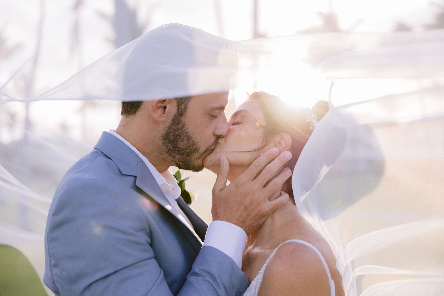 Romantic wedding portrait captured through flowing veil at sunset.
