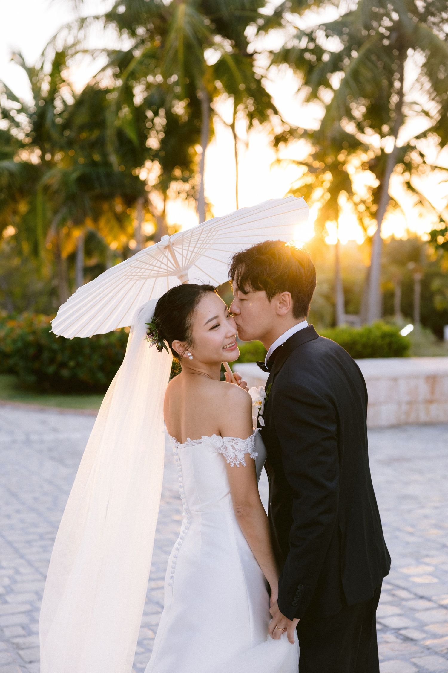 Wedding couple sharing intimate moment under white parasol at sunset.