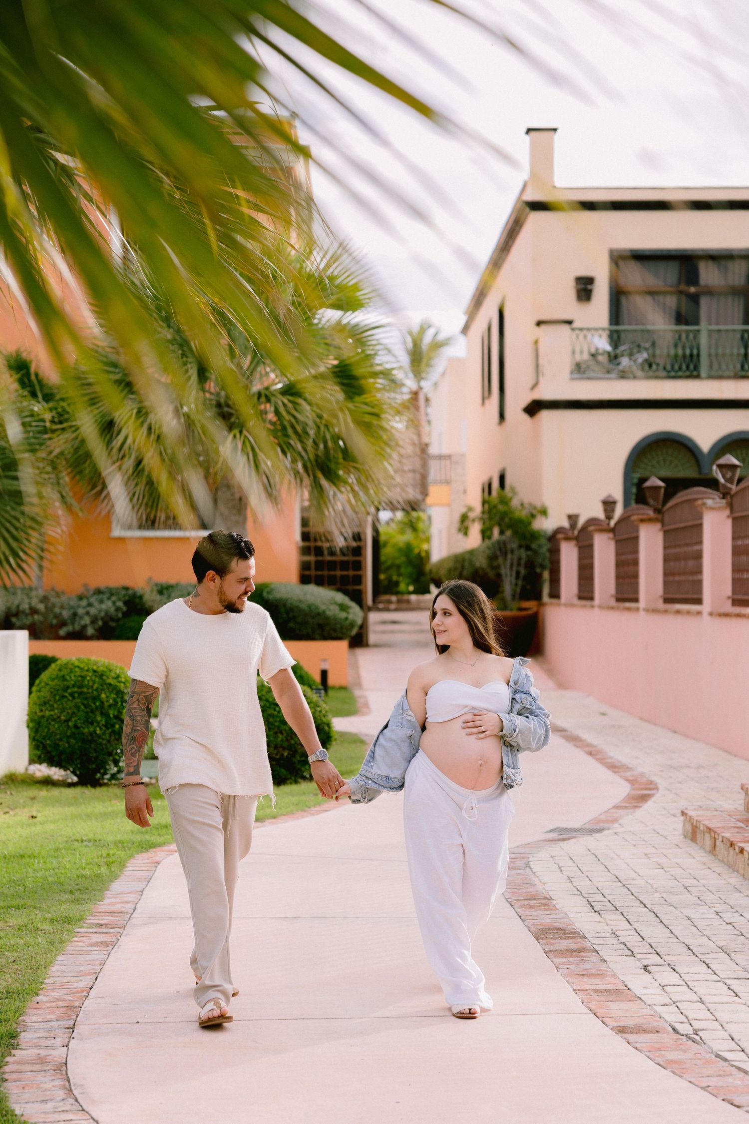 A family takes a casual stroll together along a palm-lined walkway outside Mediterranean-style buildings.