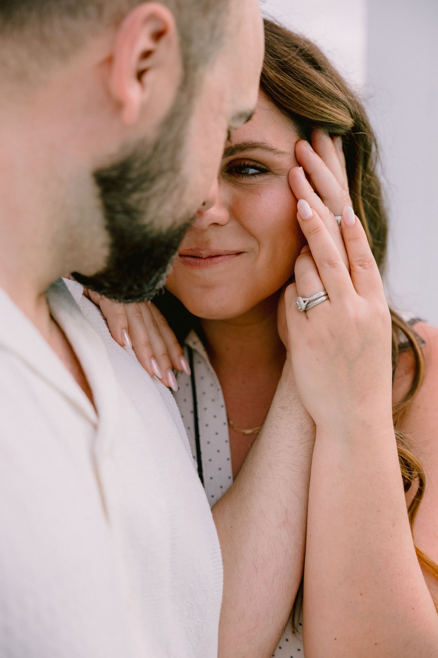Couple sharing an intimate moment, woman smiling and showing engagement ring, man with beard leaning close.