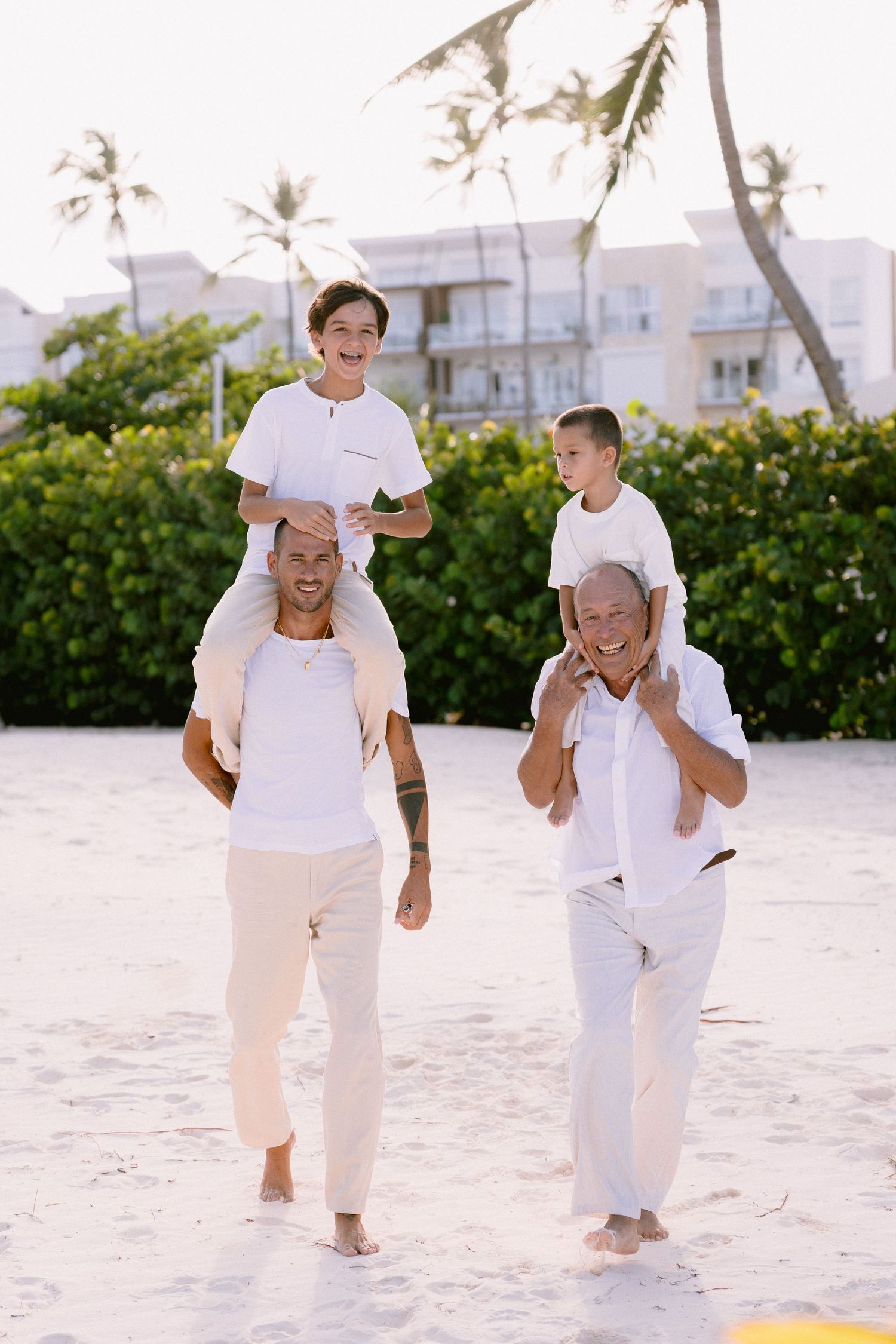 People in white clothing play and give piggyback rides on a sunny beach.