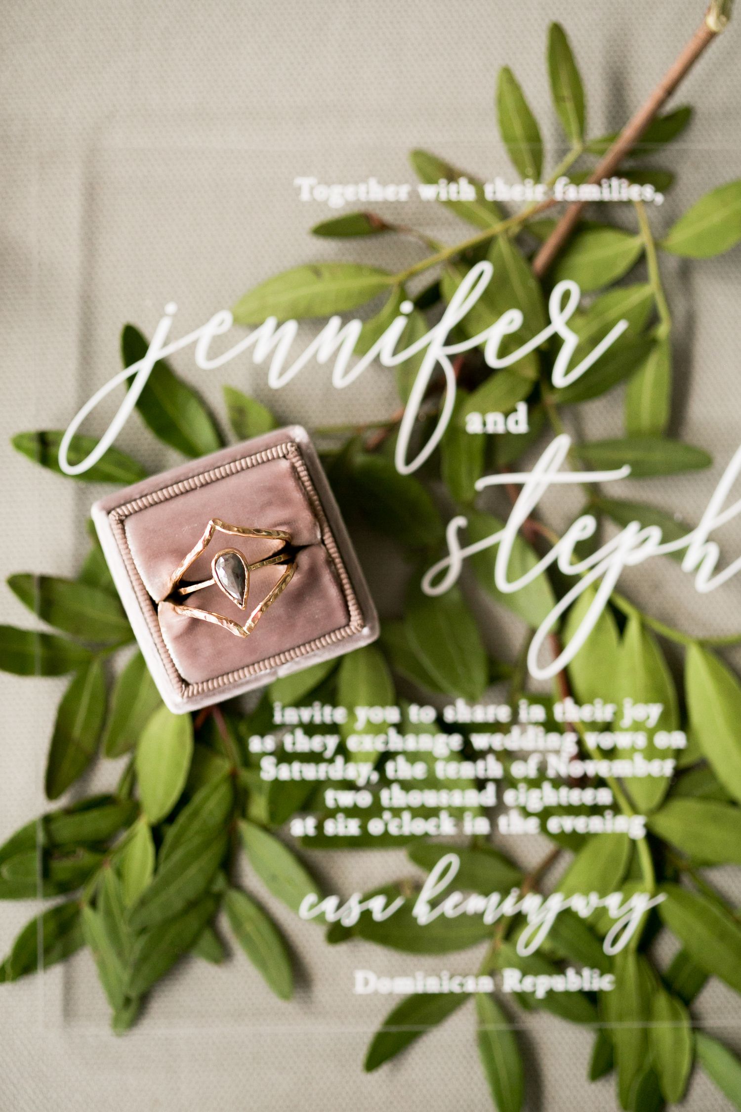 Wedding invitation details with cursive text and greenery on white background.