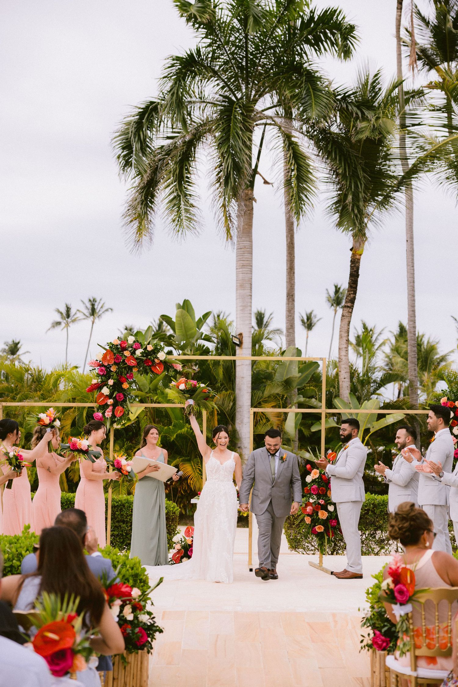 Outdoor tropical wedding ceremony with palm trees and red floral arrangements under a sunny Hawaiian sky.