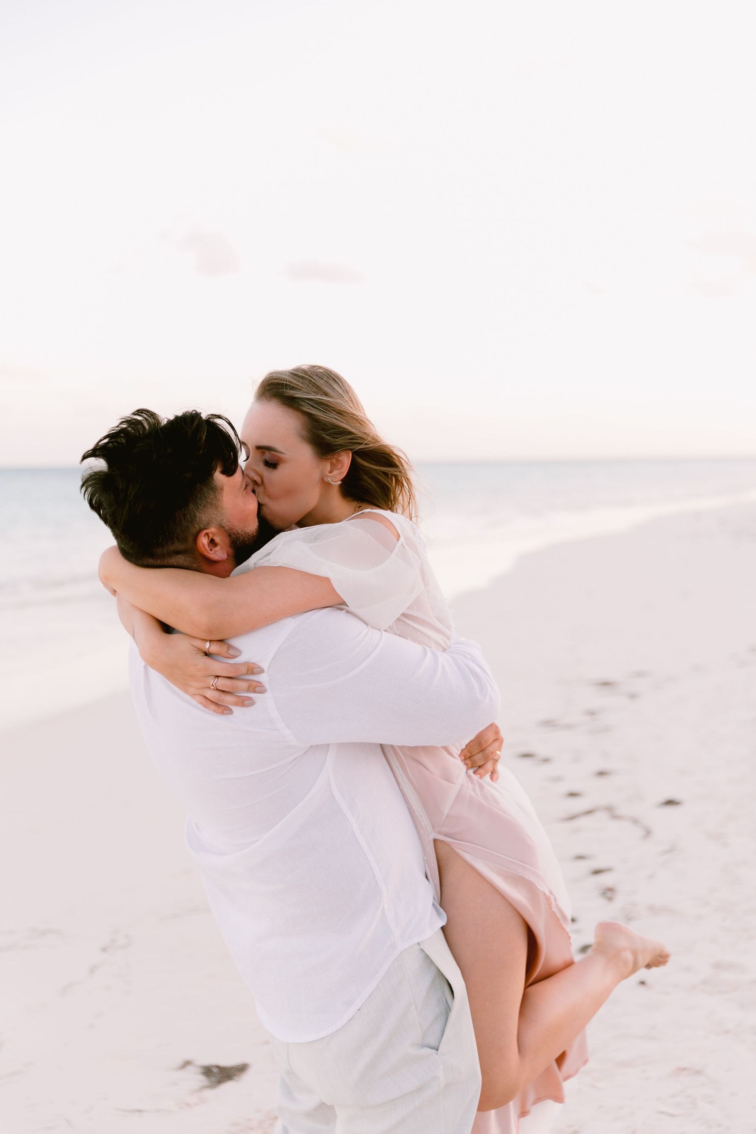 Romantic embrace between couple in white clothing on a sandy beach.