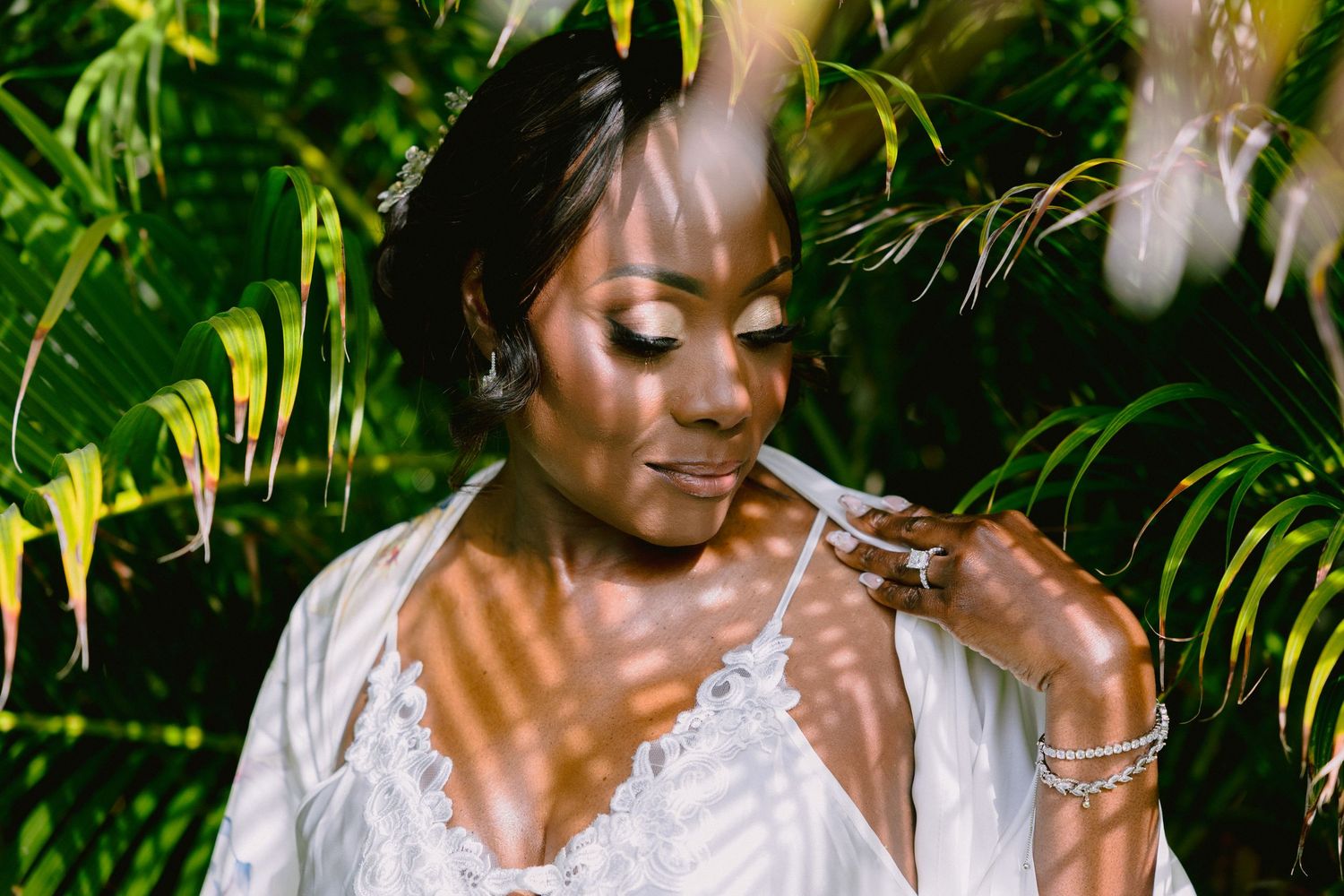 A person in a white dress laughs joyfully while surrounded by lush green tropical foliage outdoors.