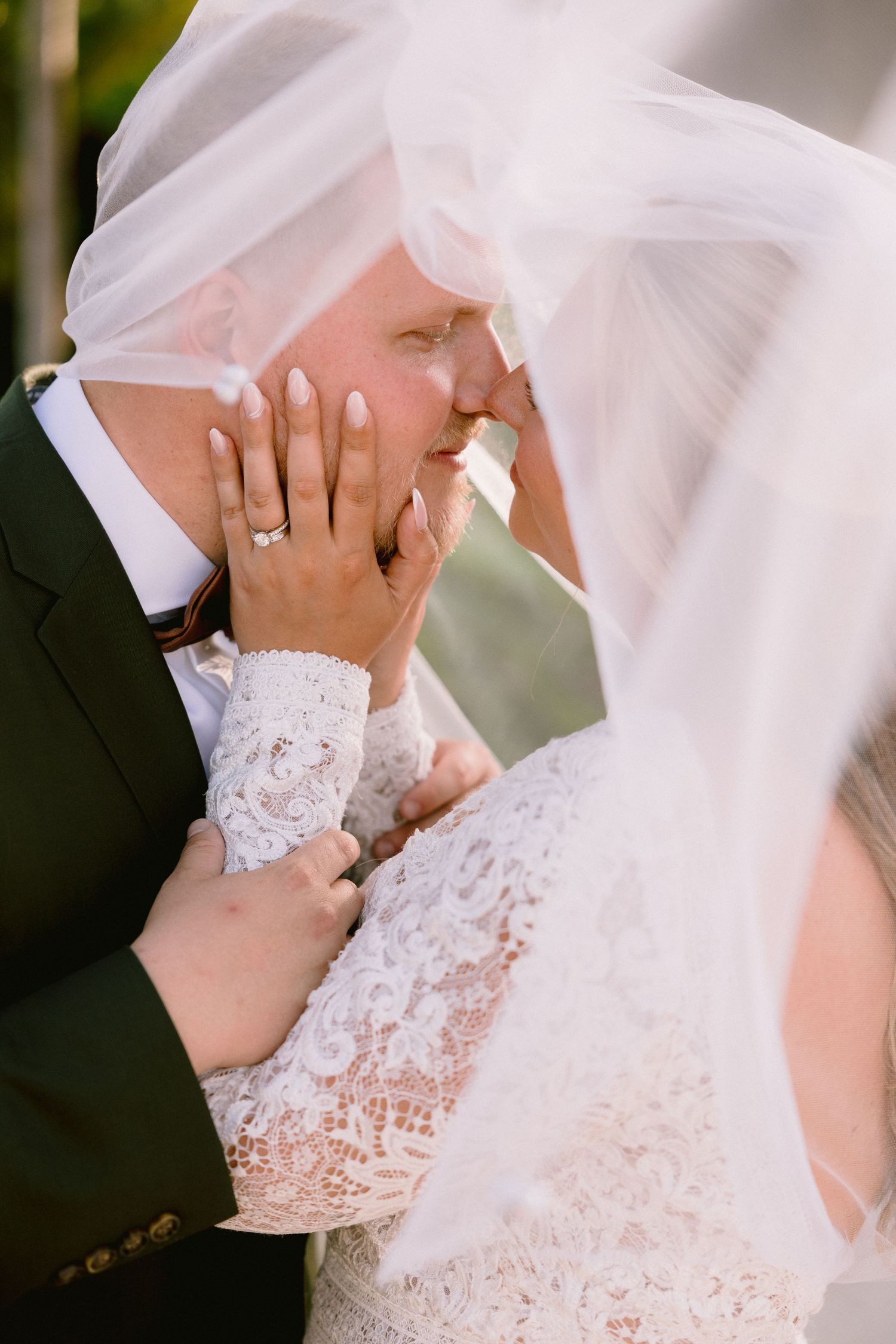 A bride and groom share an intimate kiss under a flowing white veil on their wedding day.