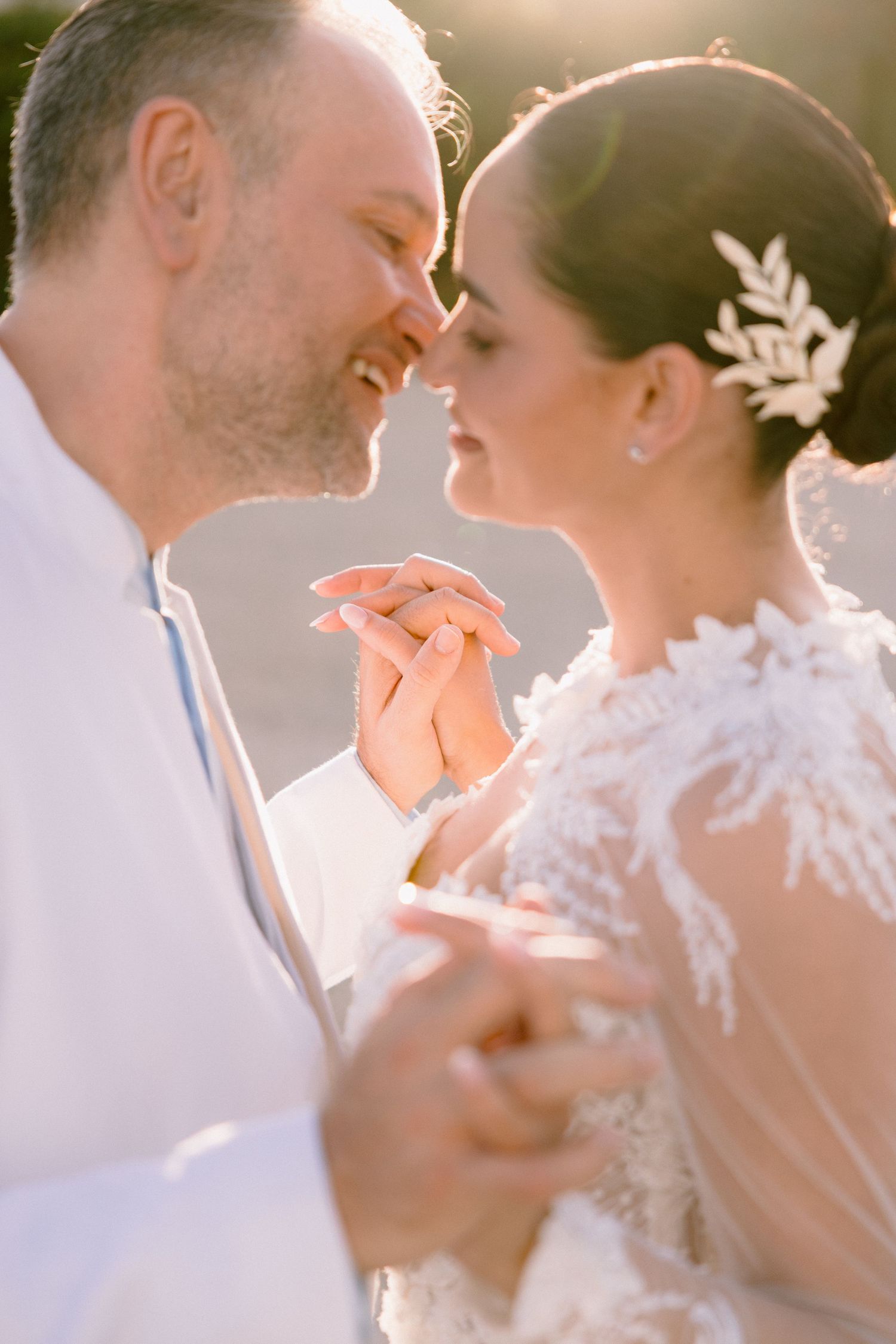 A romantic wedding couple shares an intimate moment in soft sunlight while wearing white formal attire.