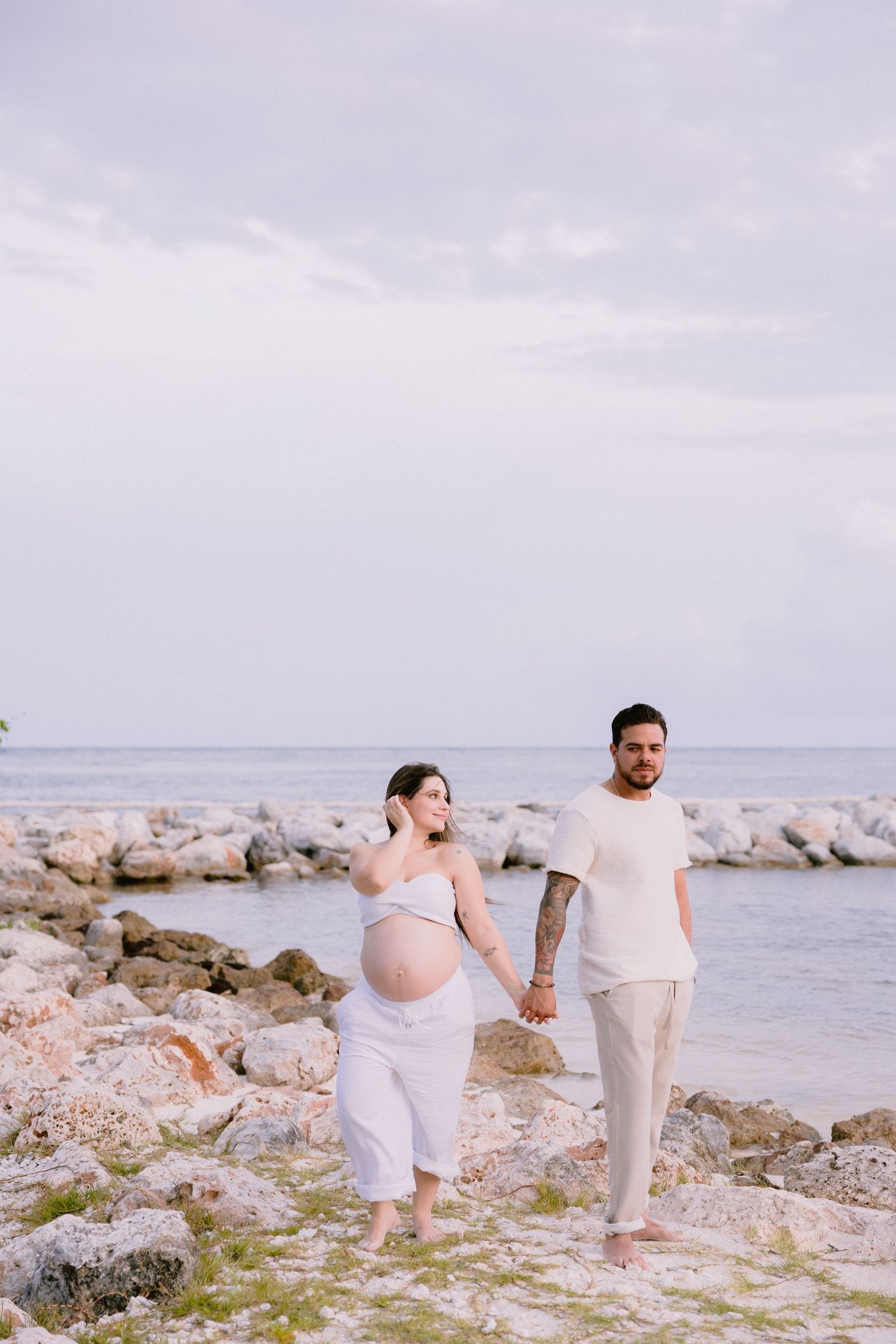 Couple in white clothing walking together along a rocky beach shoreline while exploring the coast.