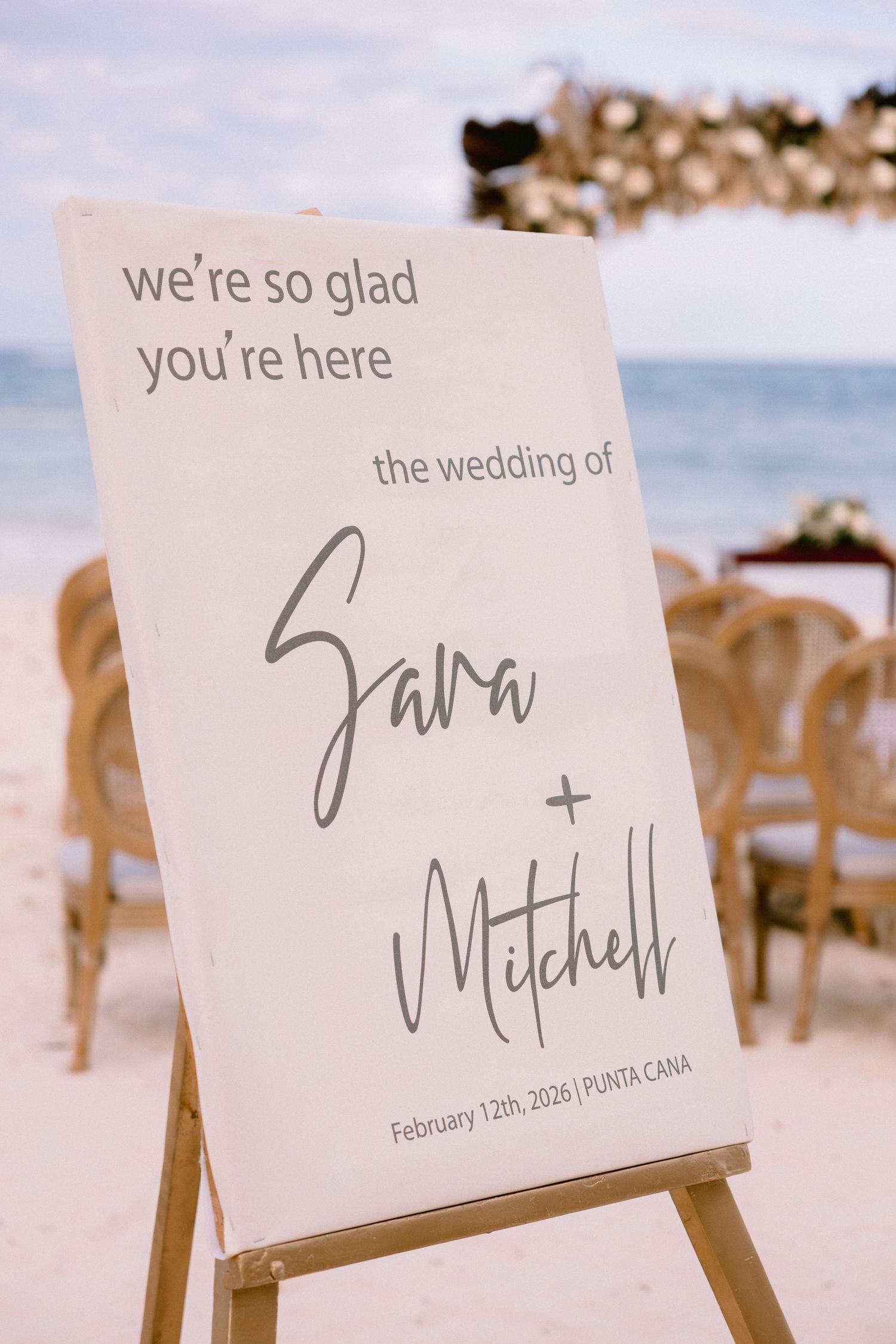 Beach wedding welcome sign for Sara and Mitchell, February 12th 2026 in Punta Cana, displayed on a wooden easel.