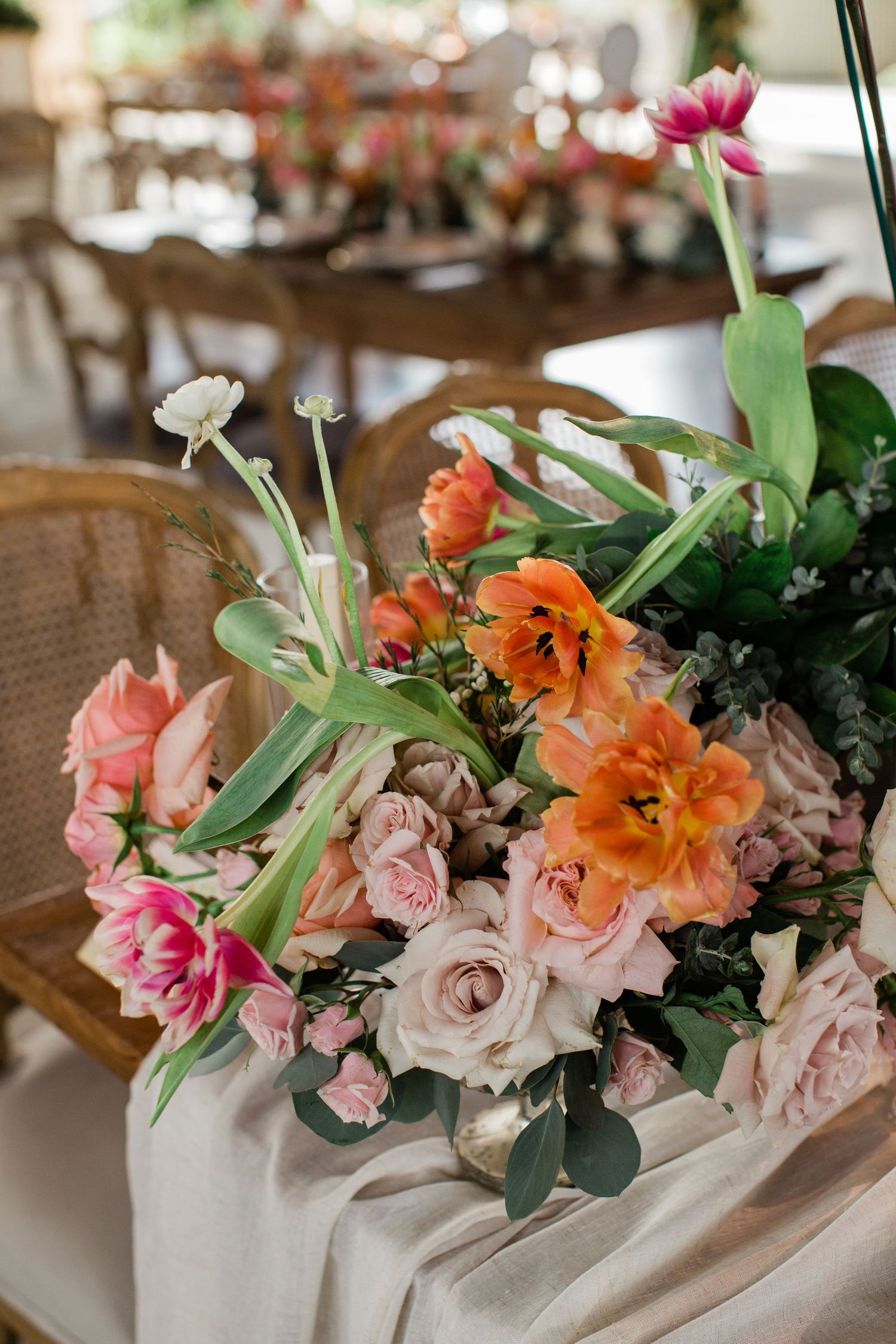 Beautiful floral centerpiece arrangement with pink roses, orange marigolds and greenery in white vases on rustic table setting.