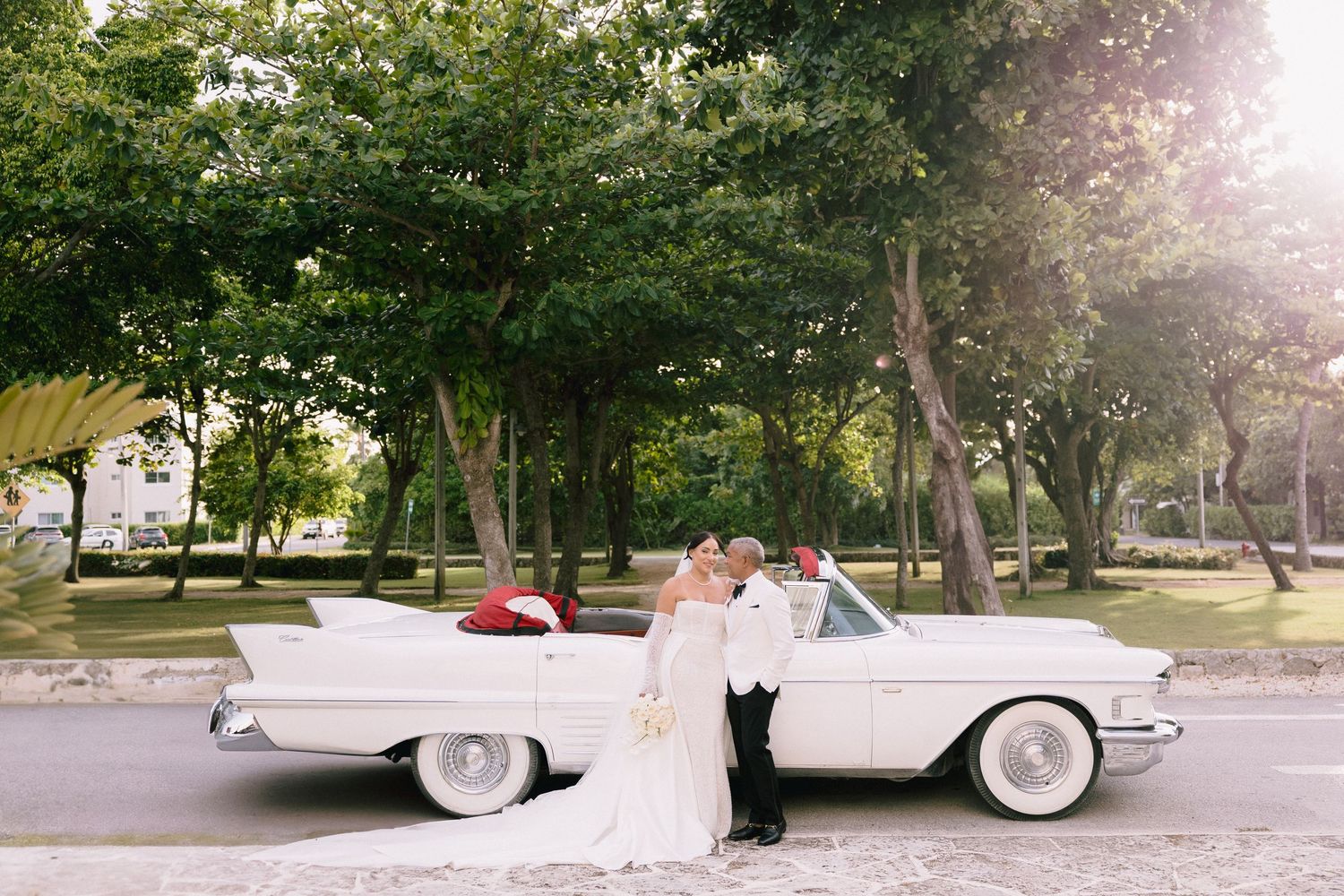 A classic white vintage car parked in a sunlit garden setting creates a romantic wedding day atmosphere.