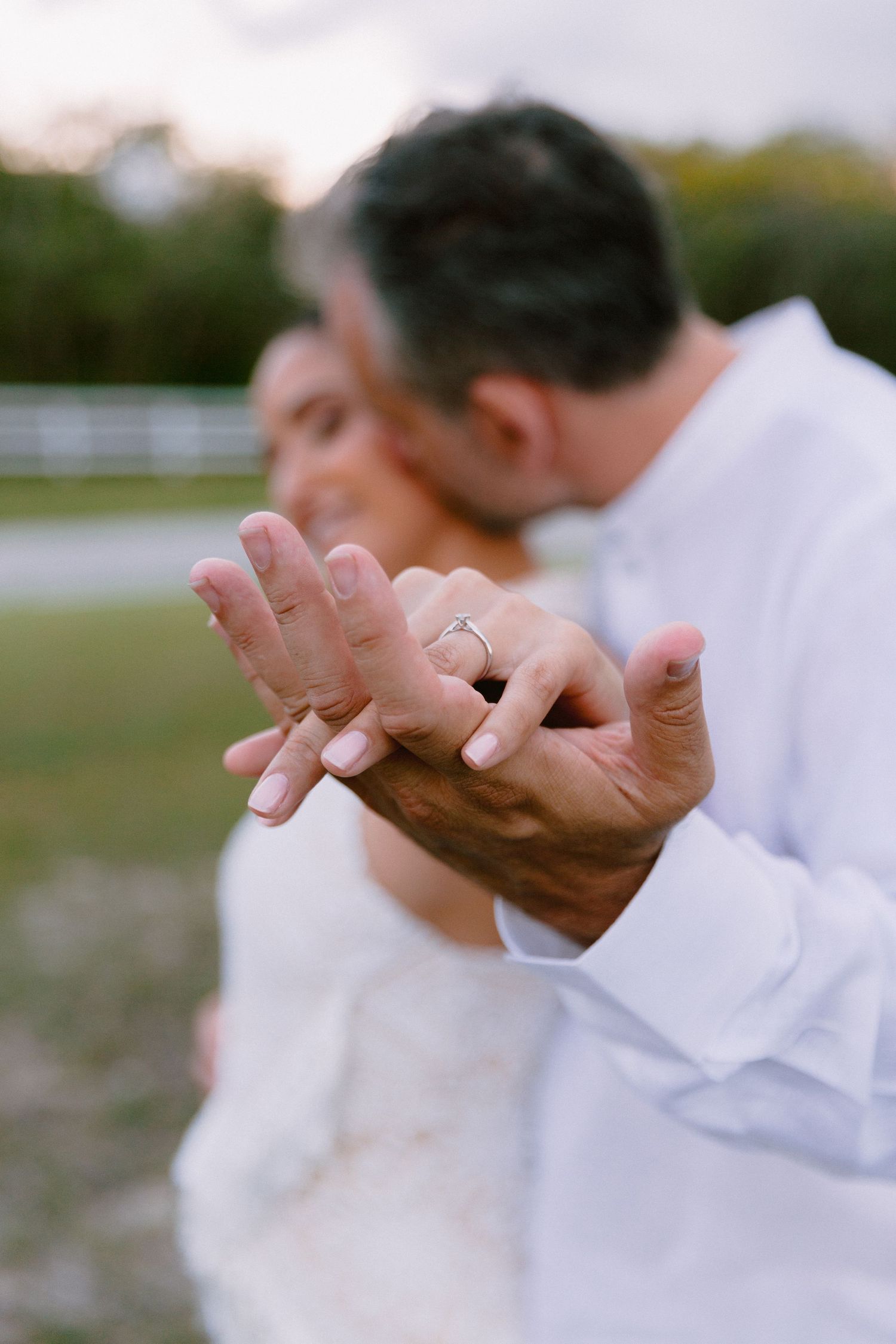 Row of guests in white clothing gesturing during an outdoor wedding ceremony.