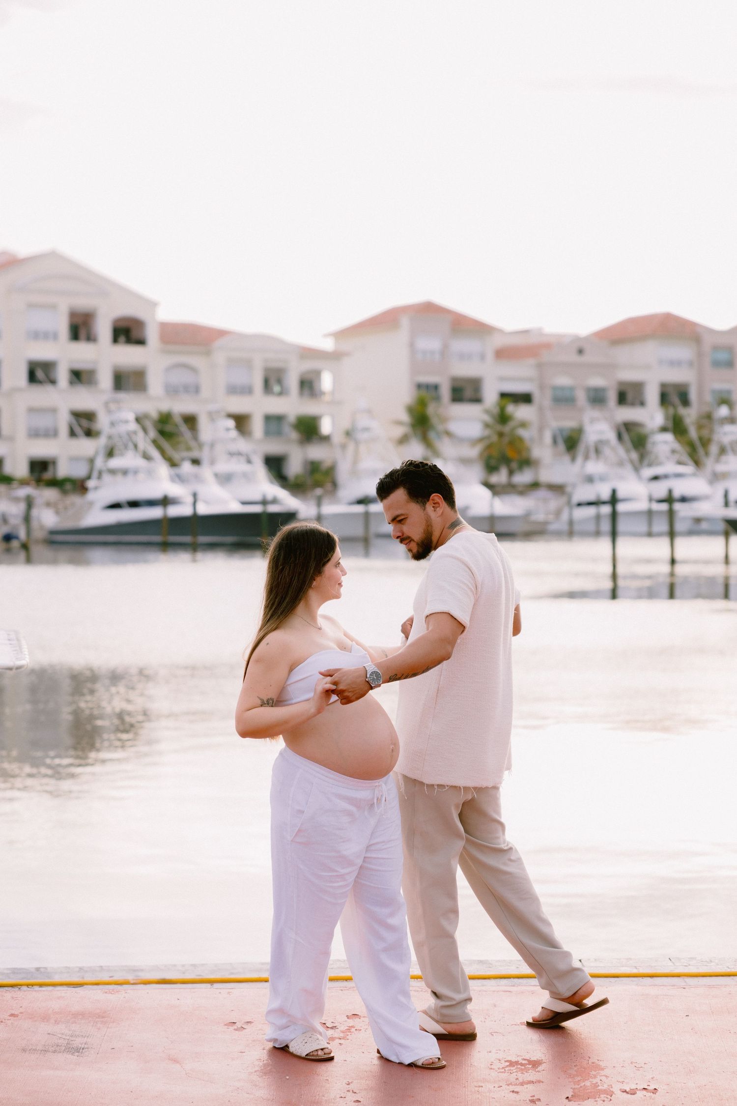A couple in white outfits dancing together in a romantic sequence by the waterfront near white buildings.