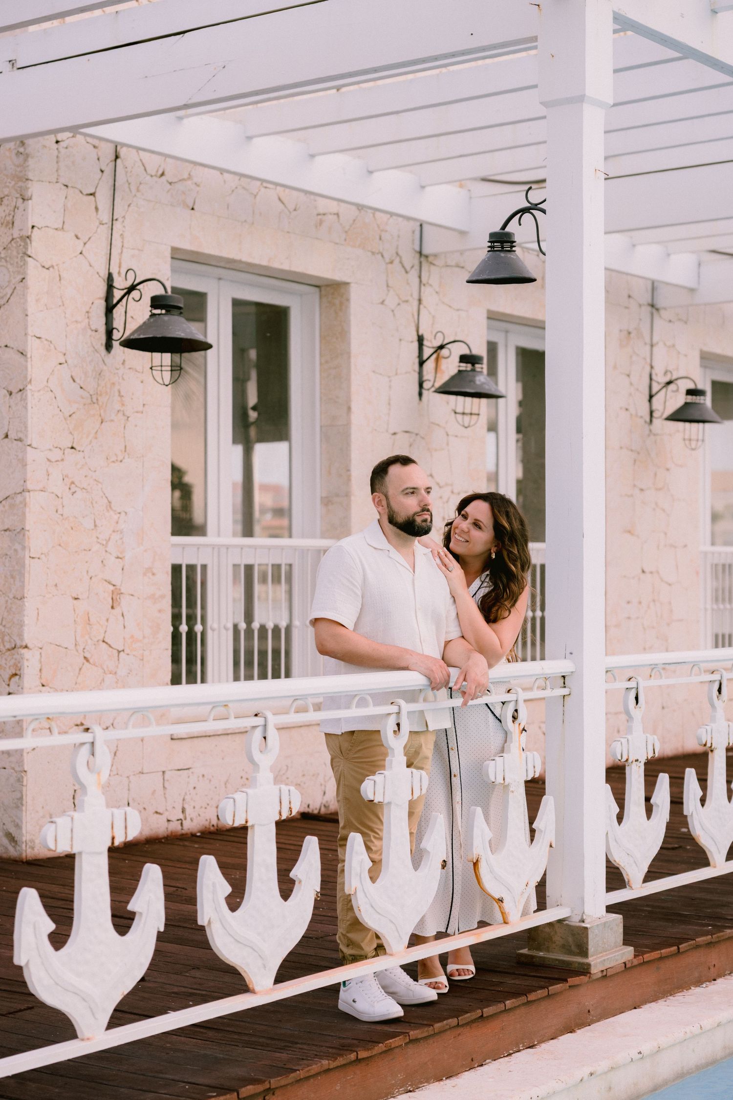 Couple embracing on a nautical-themed white anchor railing balcony at a coastal resort.