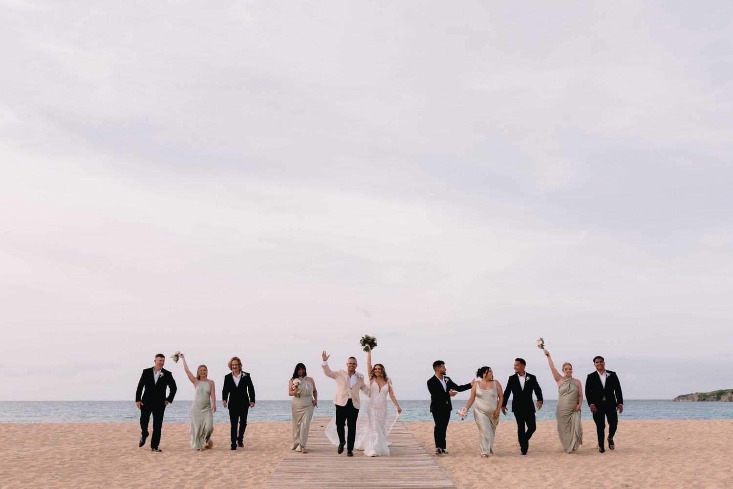 Wedding party poses together on a scenic beach with soft overcast skies in the background.
