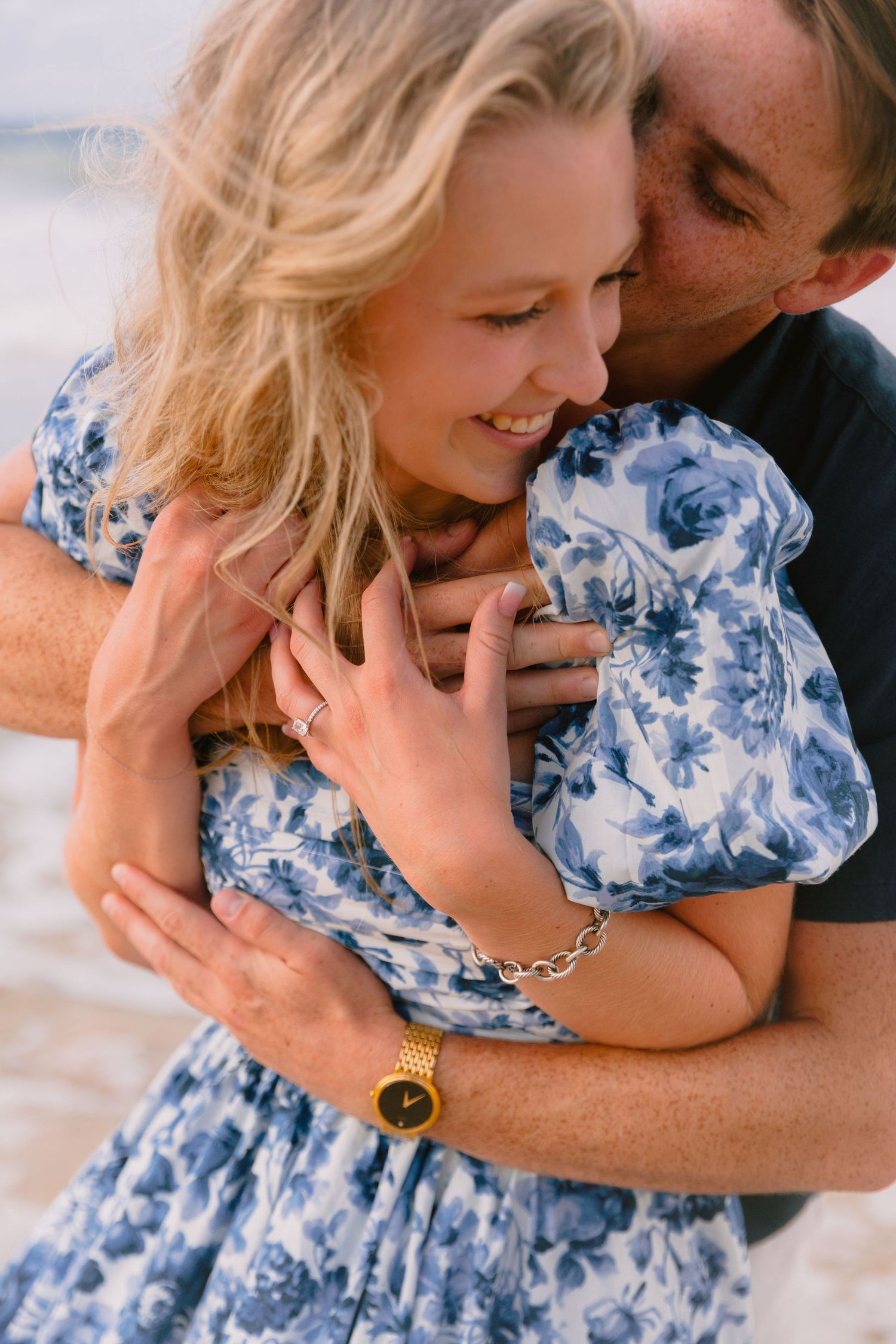 A couple in romantic embrace wearing blue and white floral dress and dark shirt lying on light colored surface.