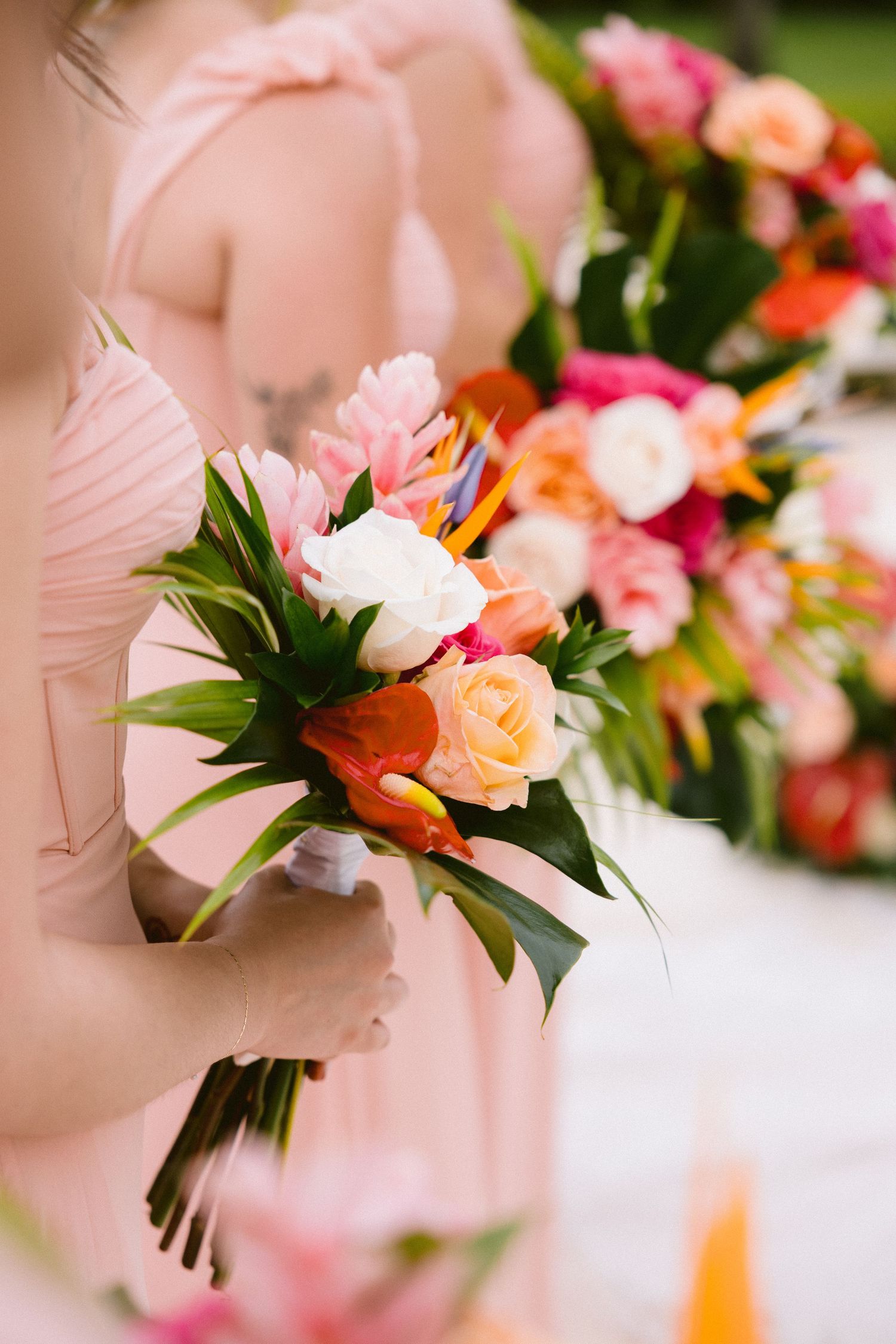 A bridesmaid holds a beautiful tropical bouquet with pink and peach roses against a soft pink dress.