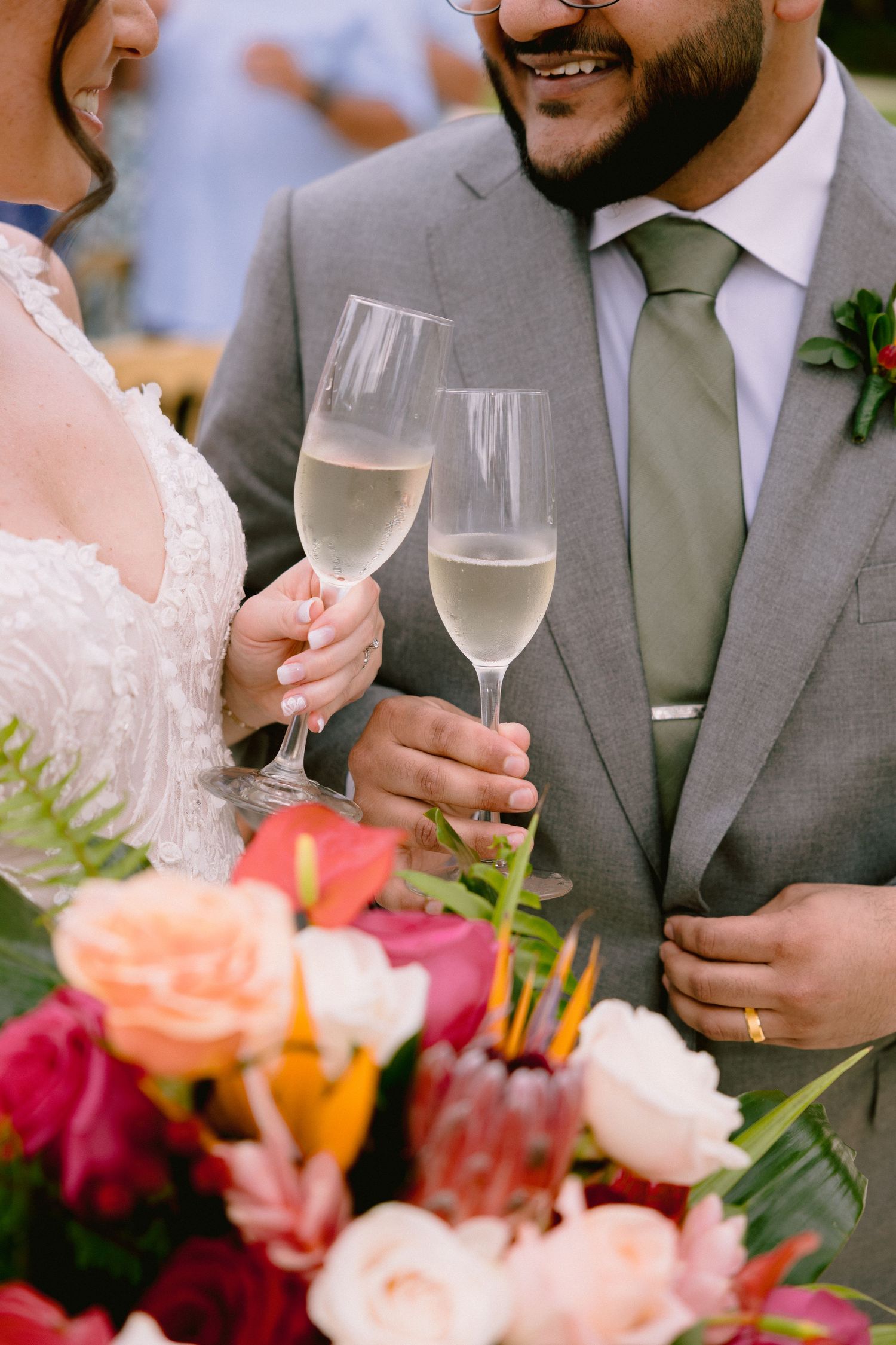 A couple toasts with champagne glasses at a wedding celebration surrounded by colorful floral arrangements.