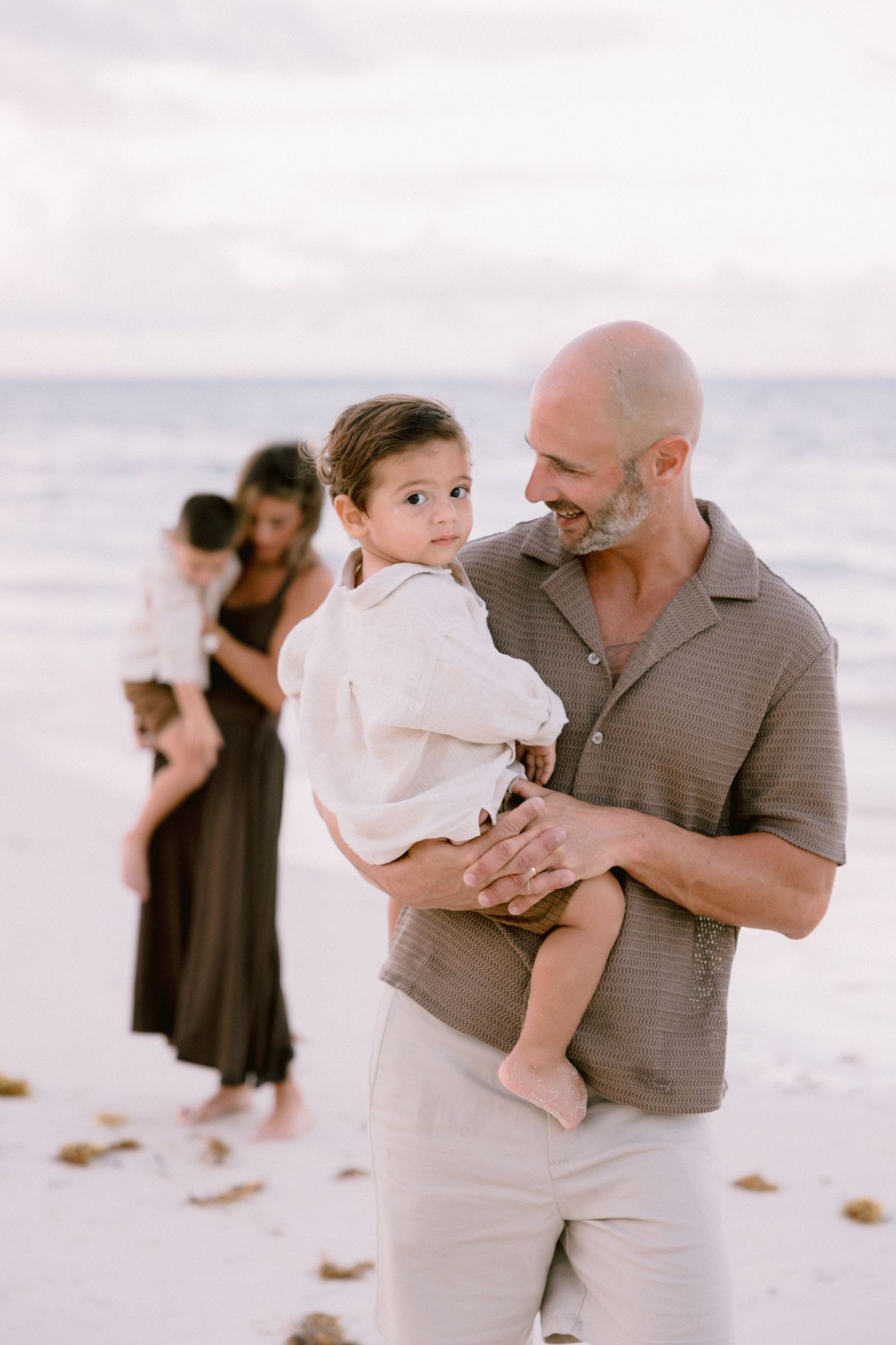 A family shares tender moments together on a white sandy beach during a photo session at sunset.