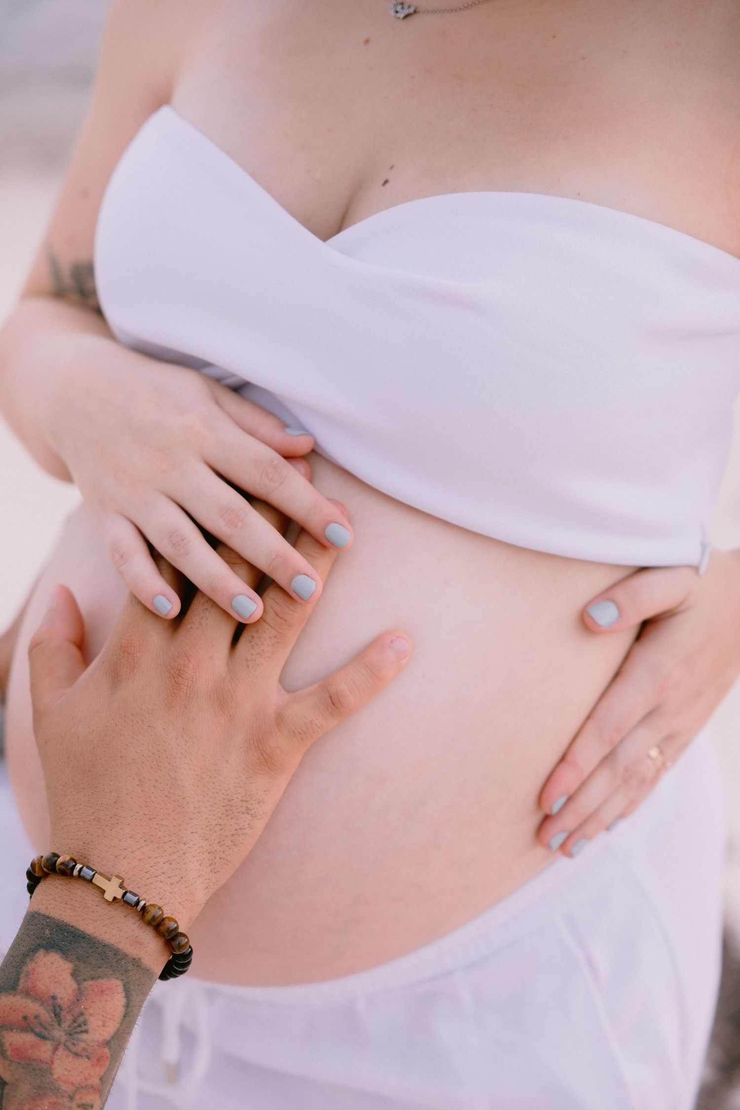 A series of images showing a pregnant belly in a white top being gently cradled by tattooed hands.