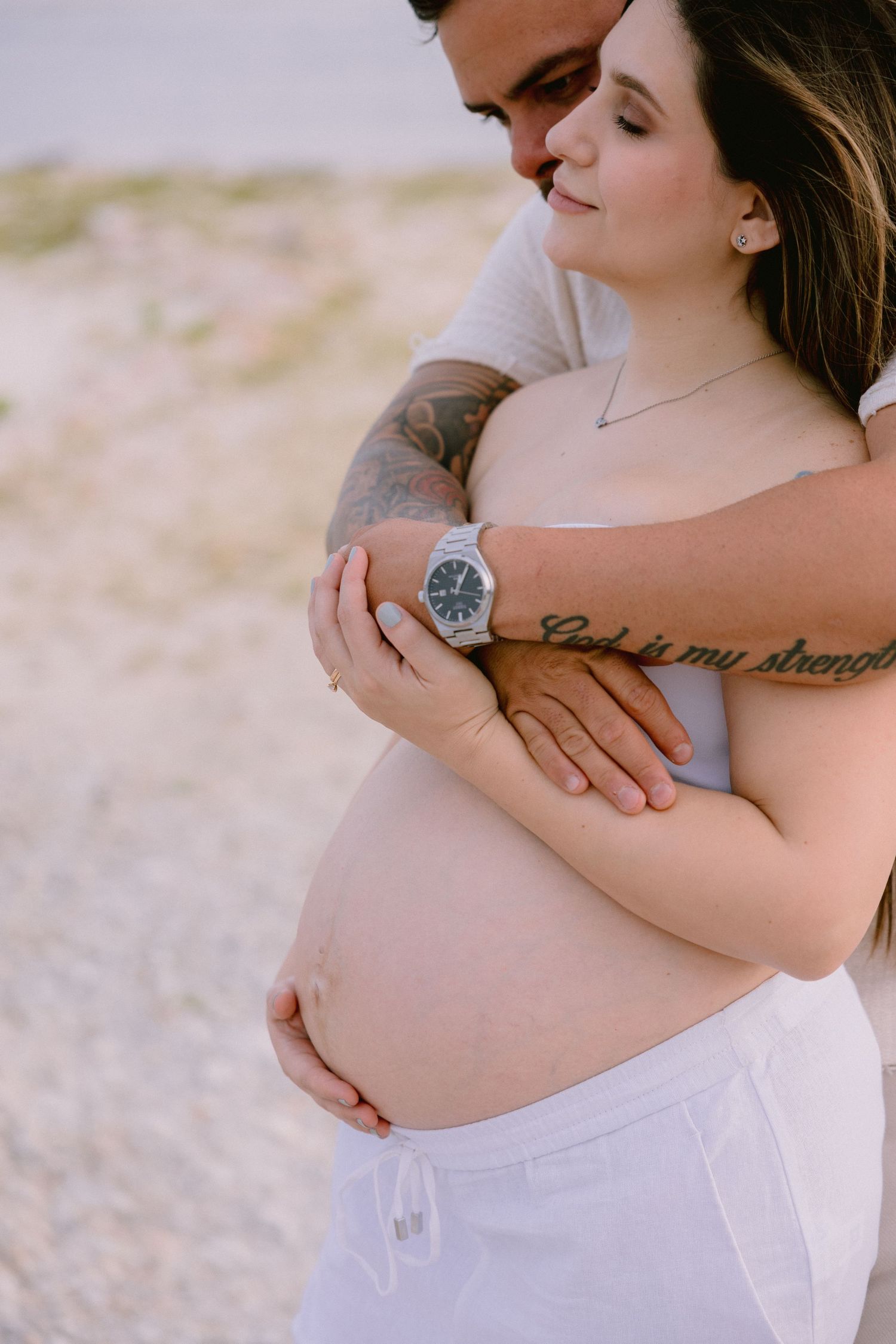 Intimate maternity photo showing hands cradling a pregnant belly against white fabric.
