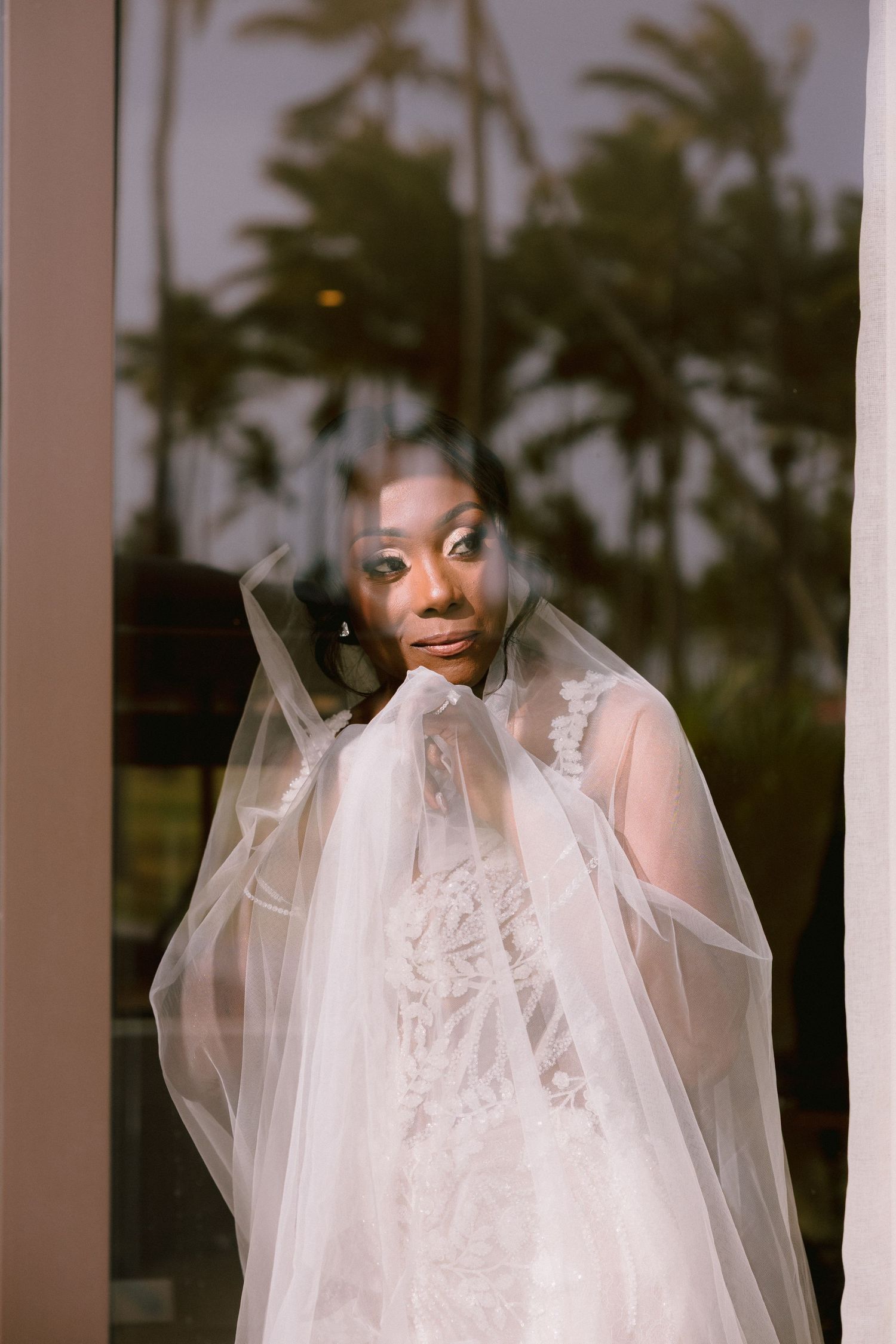 A bride in a white veil gazes through sheer tulle fabric creating an ethereal bridal portrait.