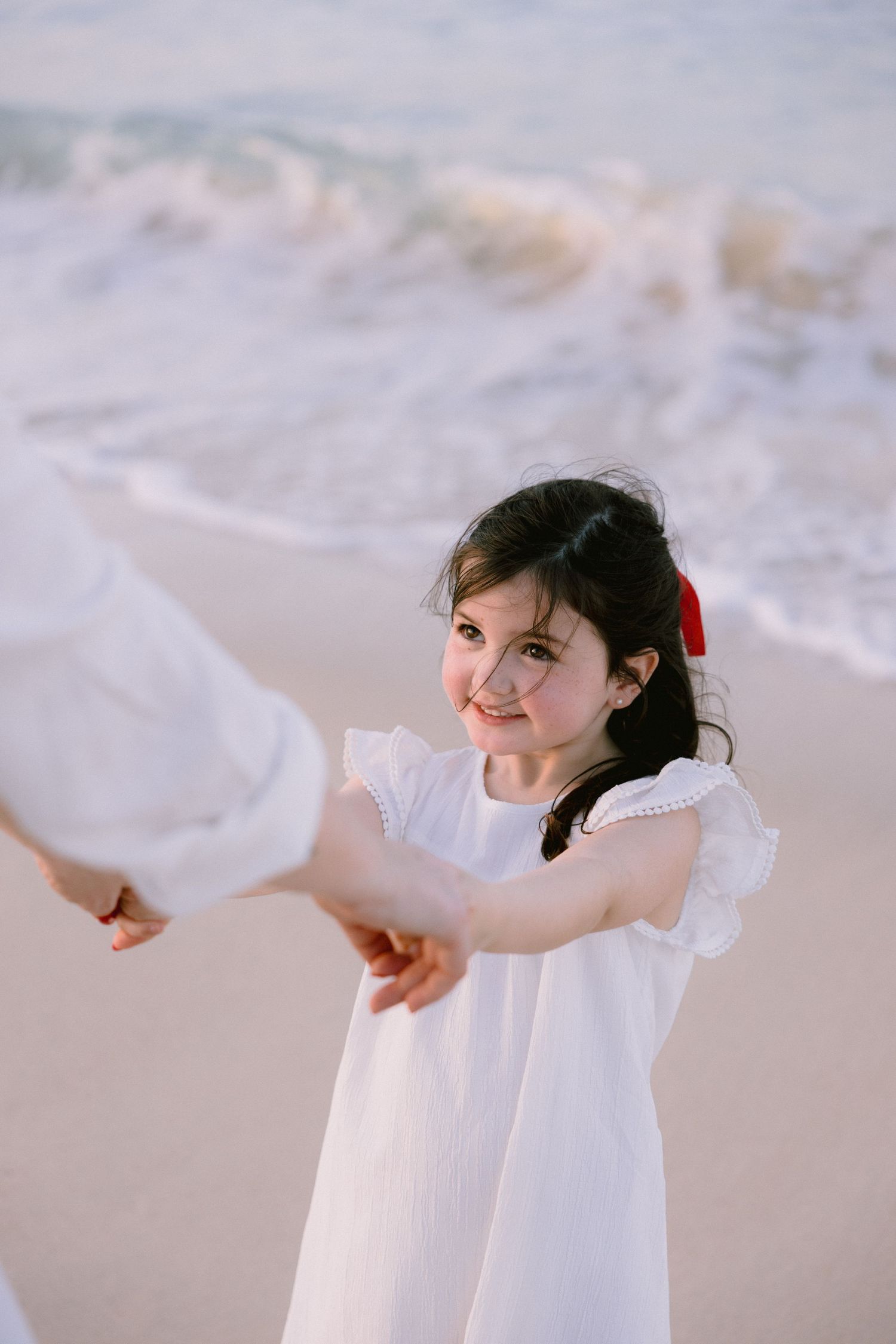 A child in a white dress holds hands with someone while playing on a misty beach.