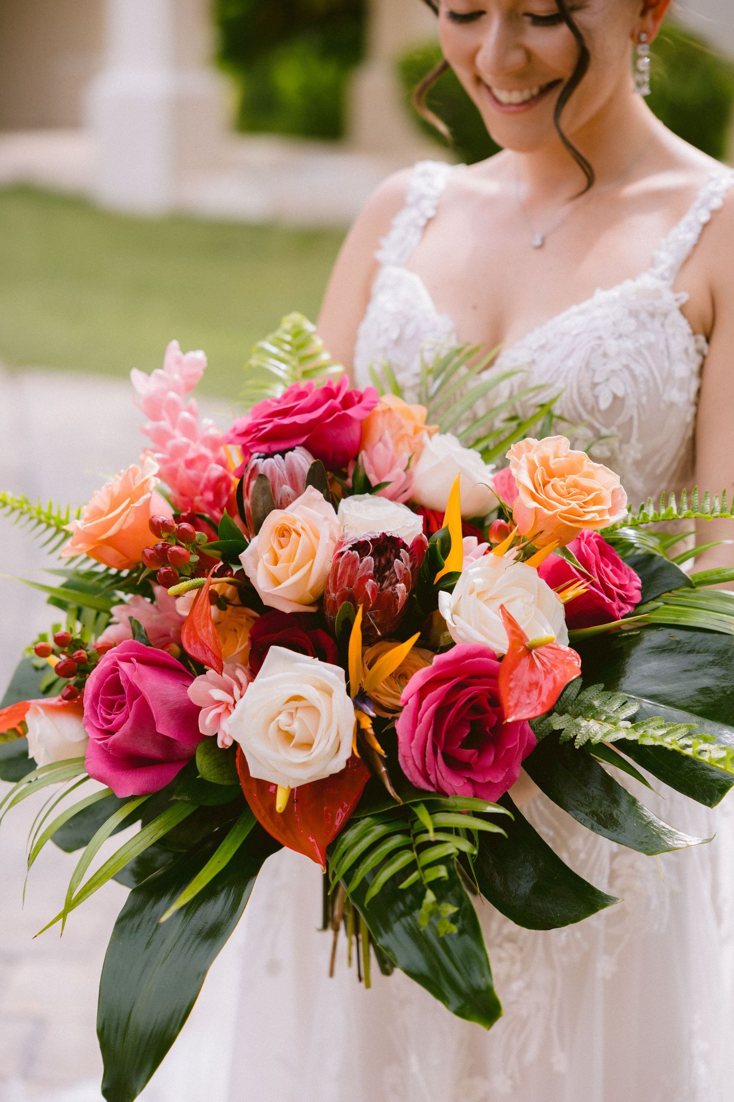 Vibrant tropical wedding bouquets featuring pink, peach and white roses with lush green foliage held against white dresses.