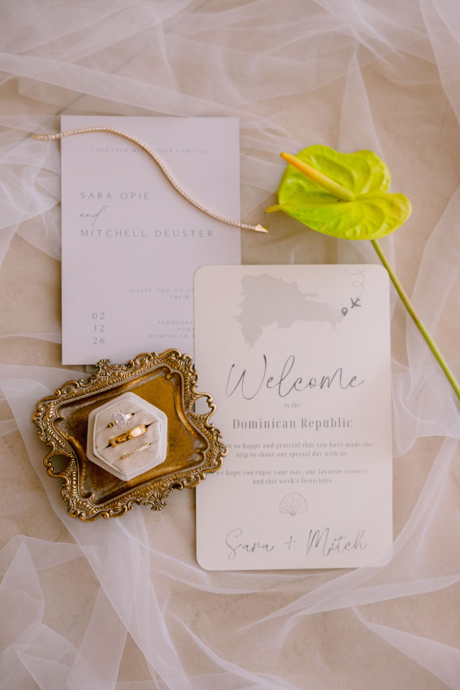 Wedding invitation suite for Sara and Mitchell in Dominican Republic, displayed with gold ring box and tropical anthurium flower.
