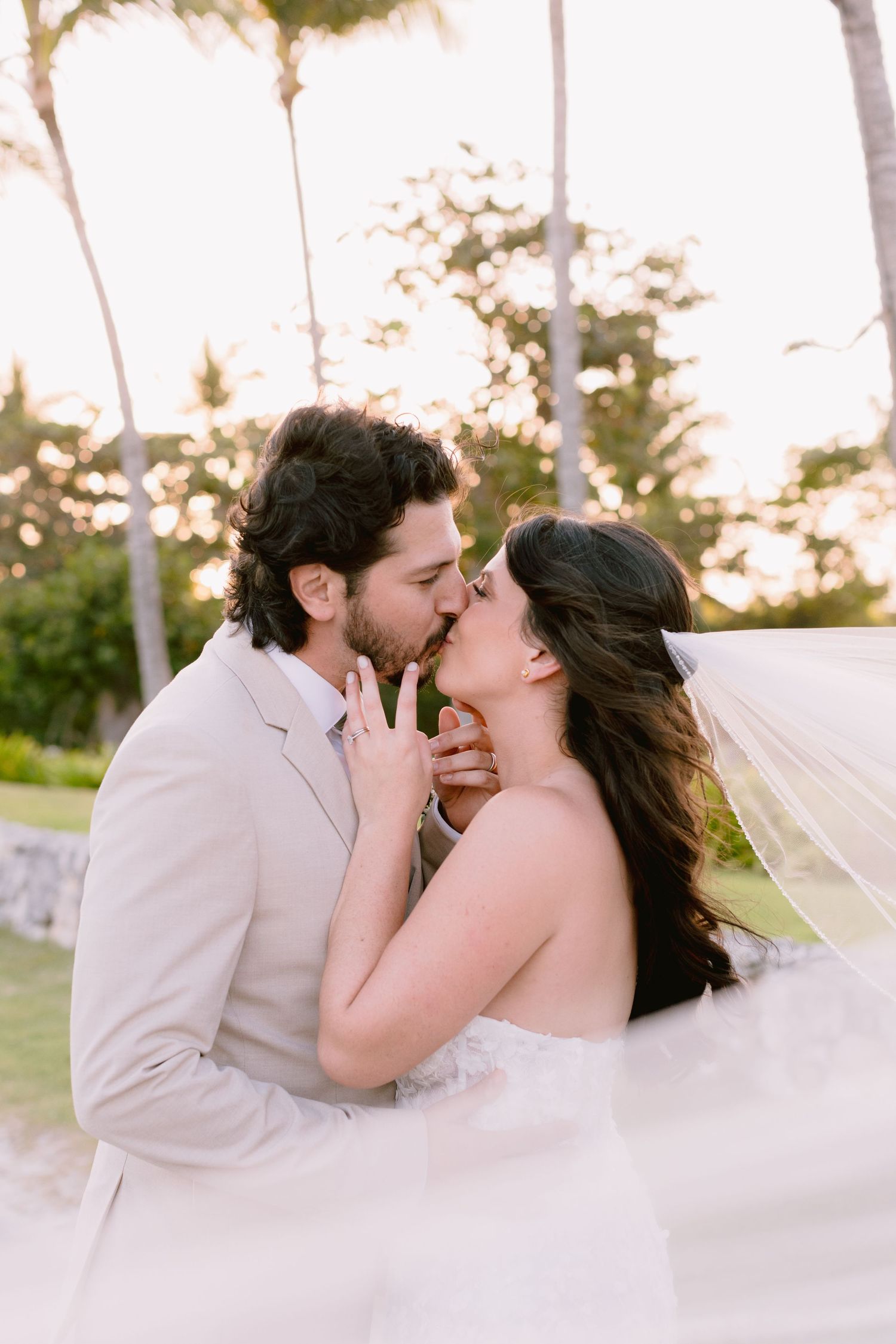 A romantic wedding moment captured in a series of four photos showing a couple kissing as a veil flows in the breeze.