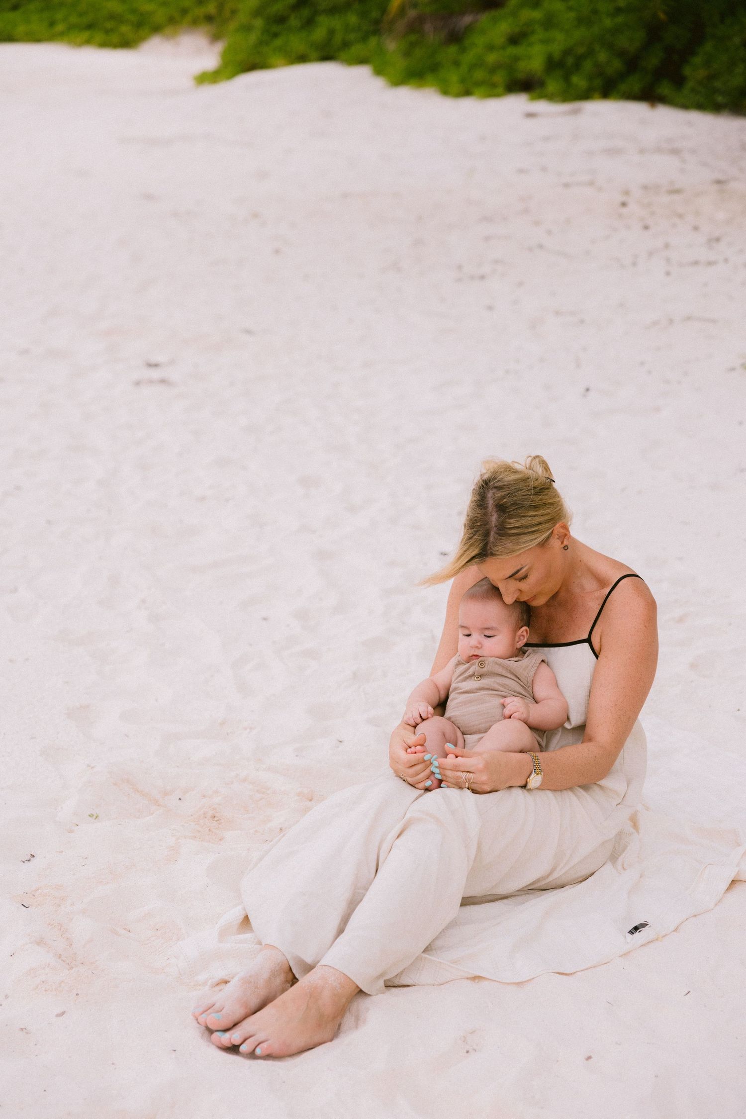 Mother and baby sharing tender moment on white sandy beach.