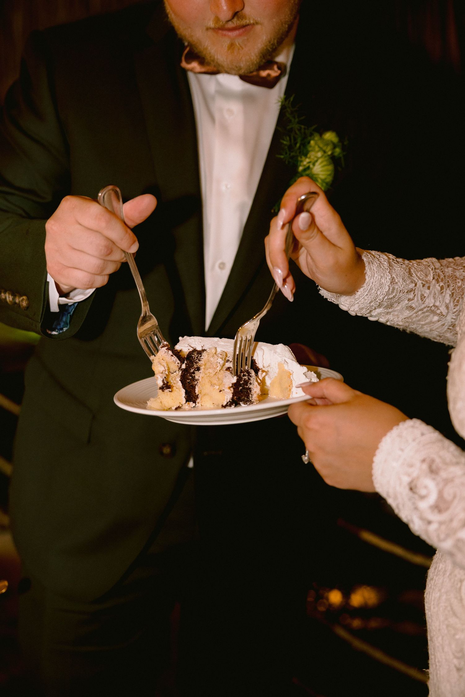 Bride and groom sharing a slice of chocolate wedding cake with forks at their wedding reception.