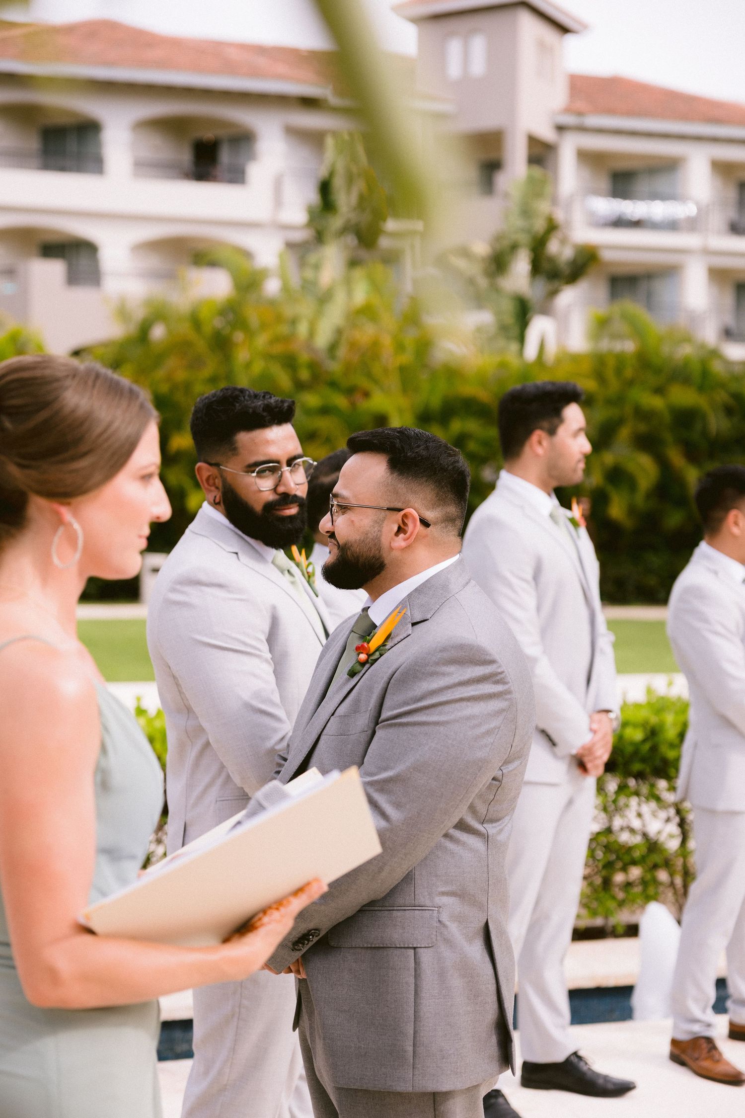 Wedding party members share emotional moments during a celebration at an outdoor venue with white buildings.