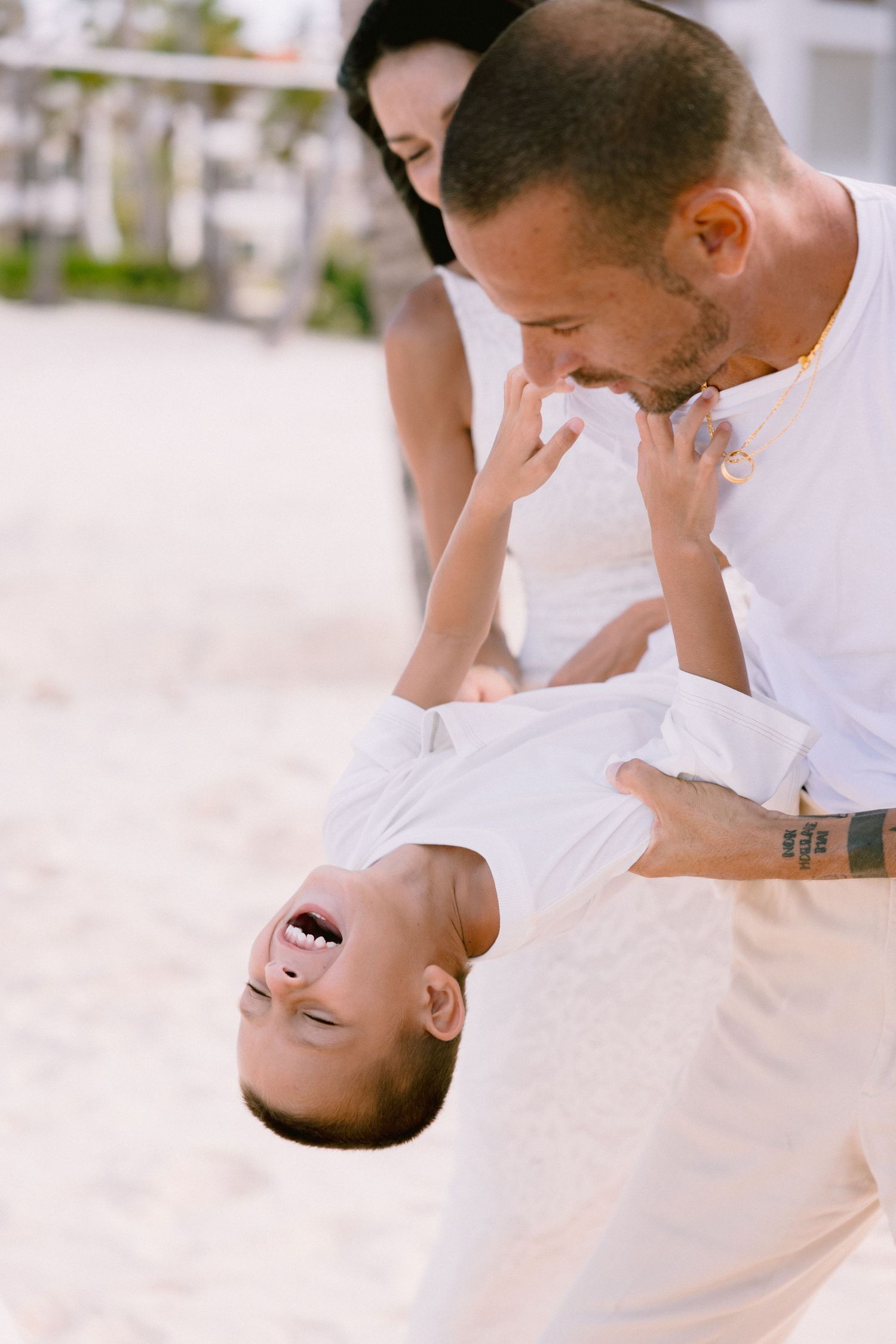 Playful dip pose between two people wearing white on a sunny beach.