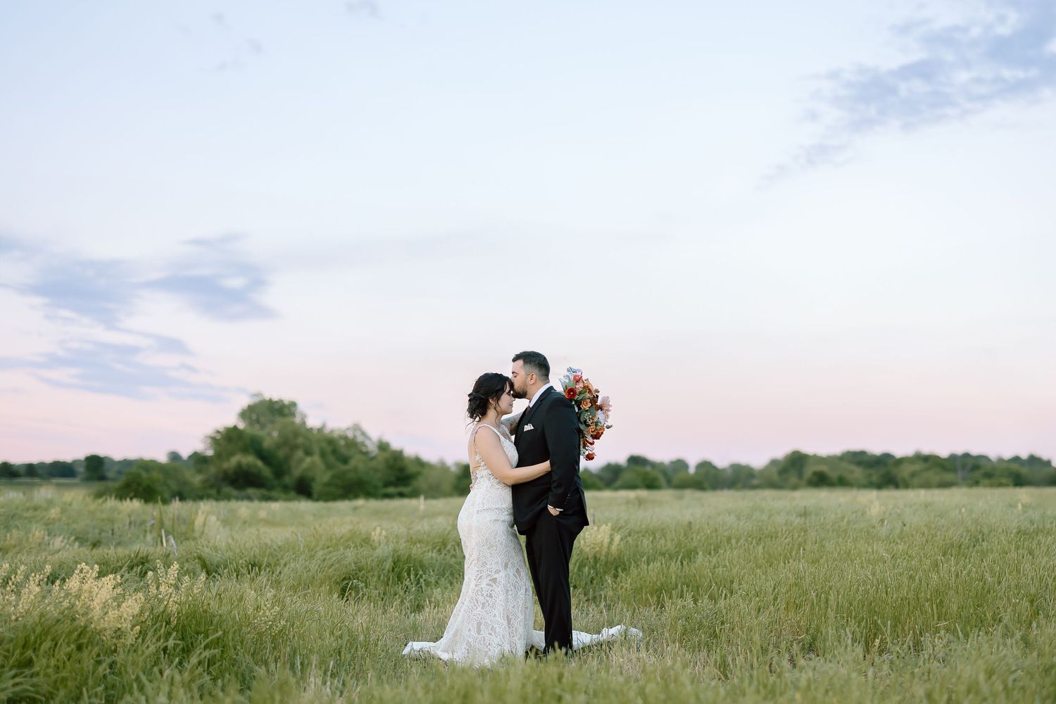 A couple poses for romantic wedding photographs in a lush green prairie at sunset.