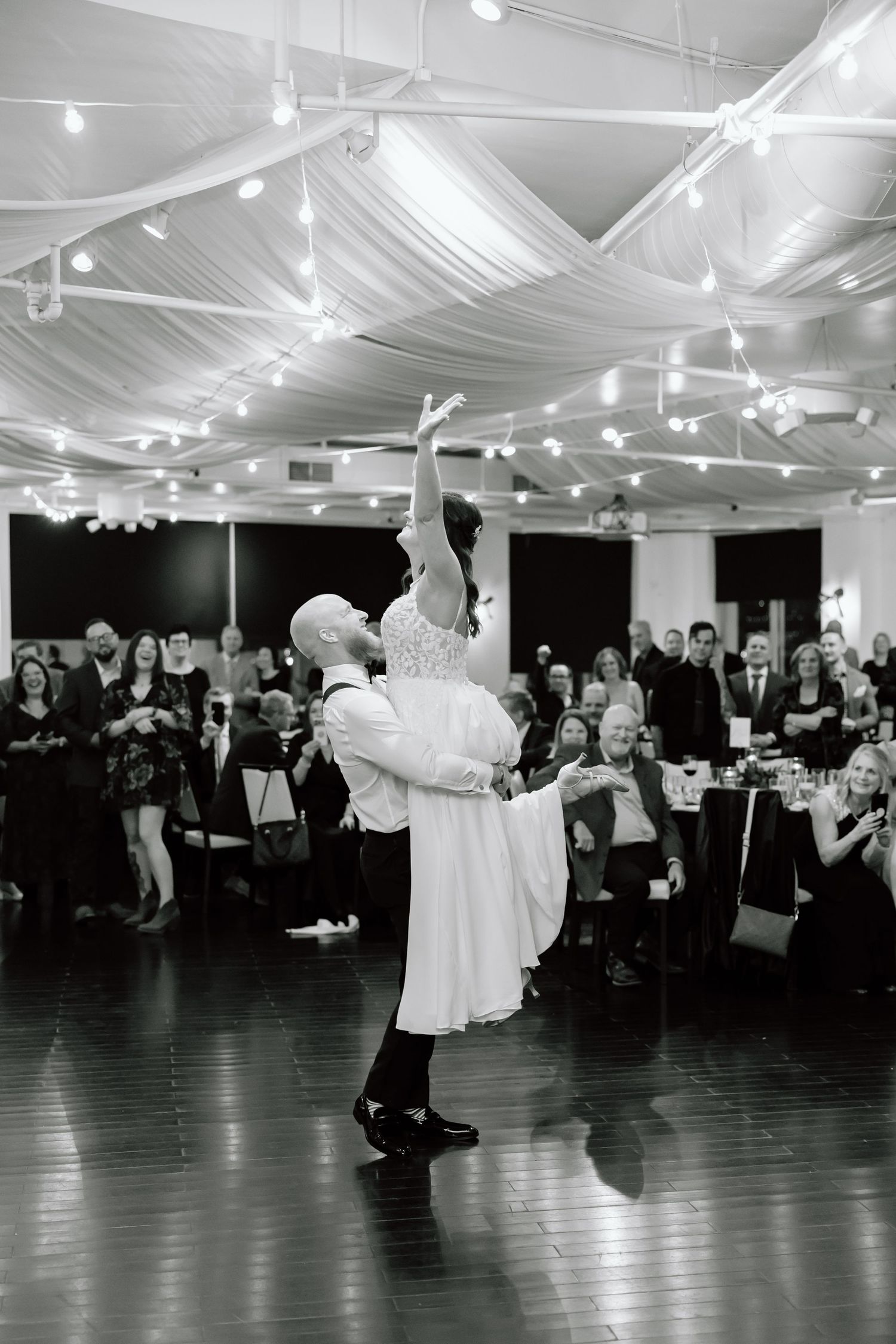 Black and white sequence of a couple dancing at a wedding reception under draped fabric and string lights.