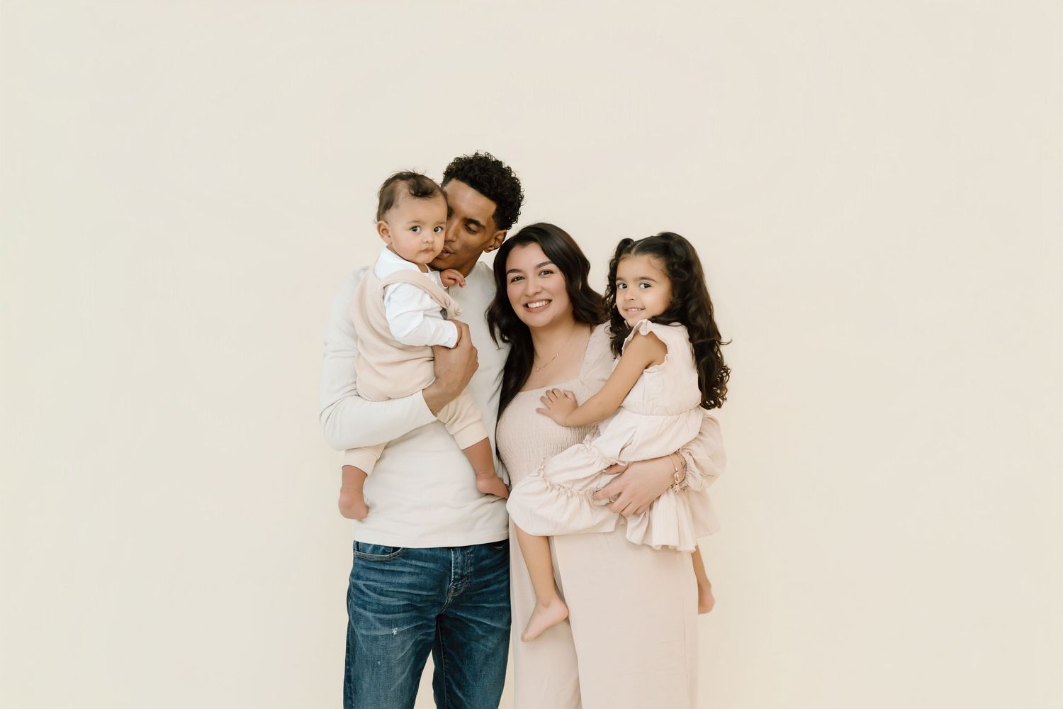 A family in neutral colored outfits poses together against a light beige background for a minimalist portrait session.